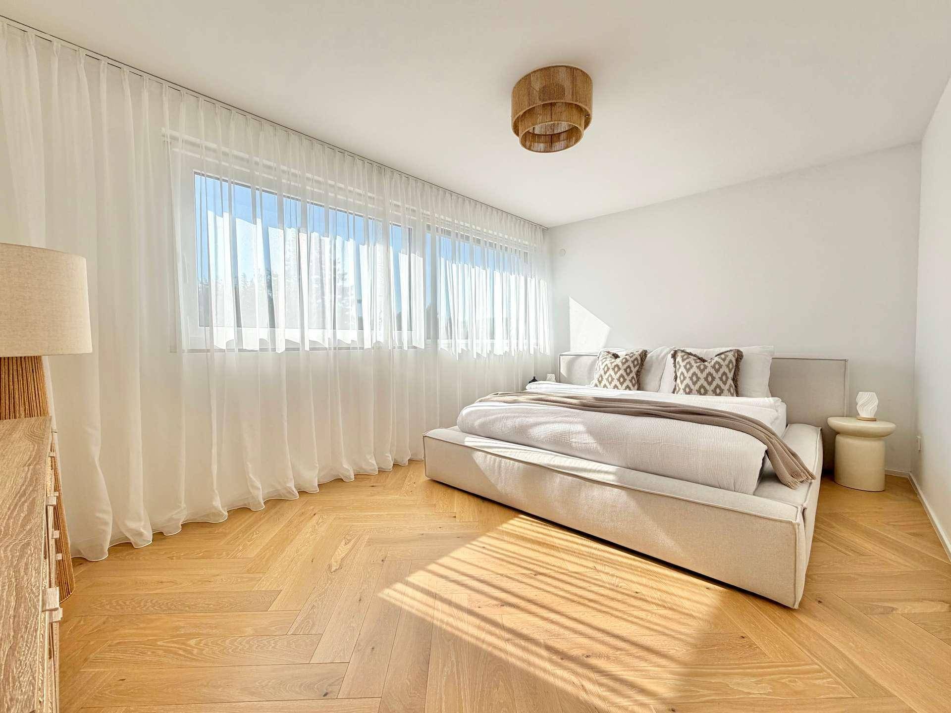 Helles Schlafzimmer mit großem Fenster, Fischgrätparkett und modernem, niedrigem Bett.