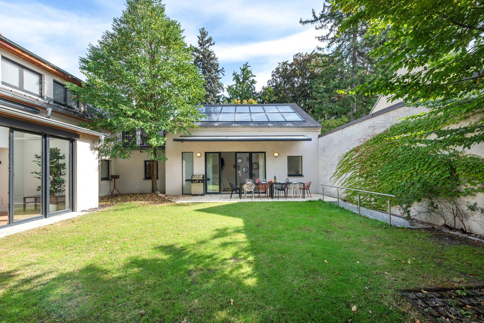 Gepflegter Garten mit Rasenfläche und einer möblierten Terrasse für Mahlzeiten im Freien.