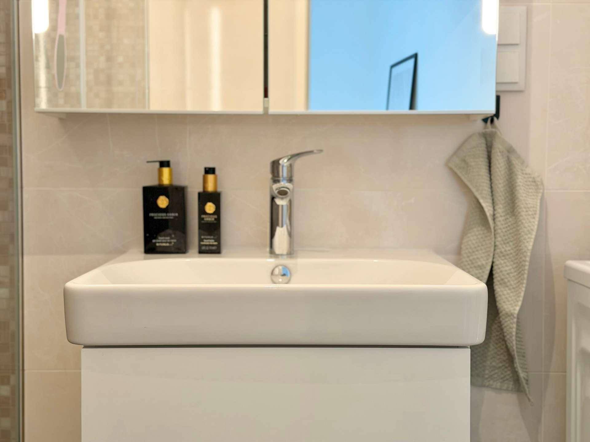 Detailansicht des modernen Waschbeckens mit Armatur und Spiegelschrank im Badezimmer.