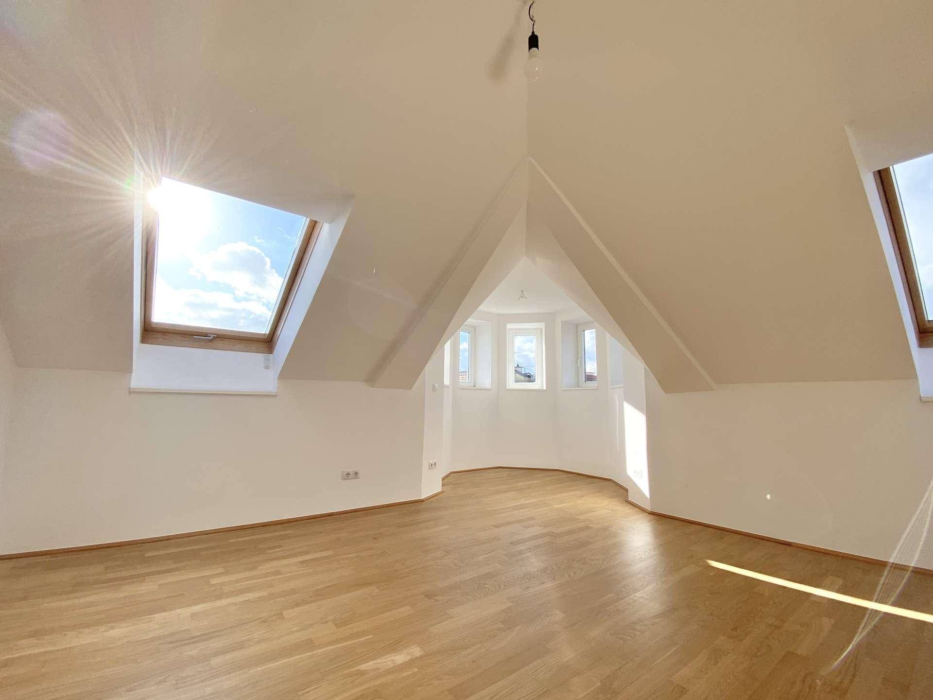 Großes, helles Zimmer mit Holzfußboden, schrägen Wänden und mehreren Dachfenstern.