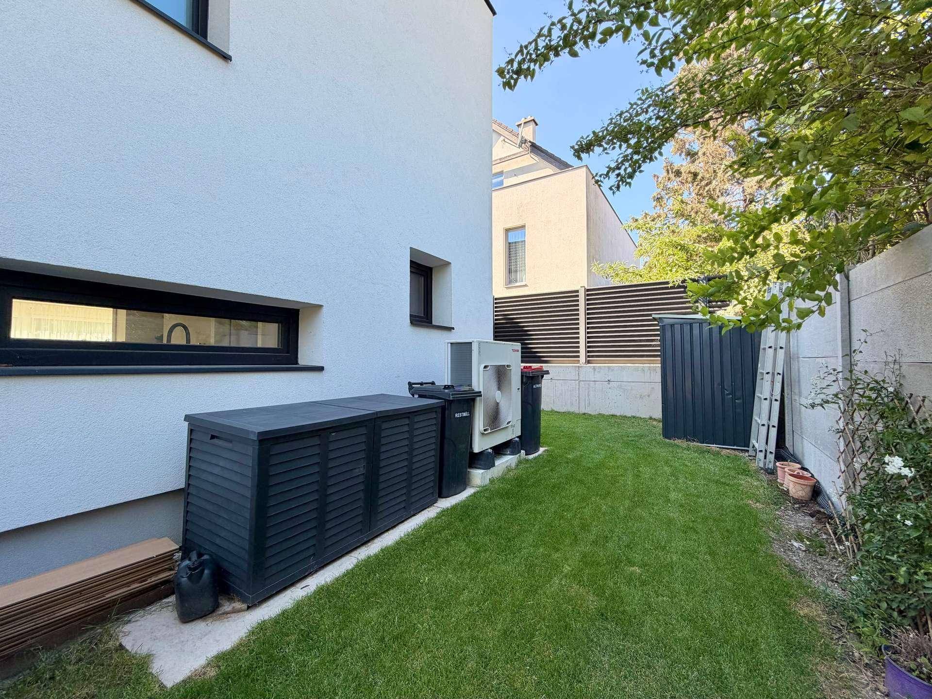 Seitlicher Gartenbereich mit Rasenfläche, Geräteschuppen und Technikinstallationen am Haus.