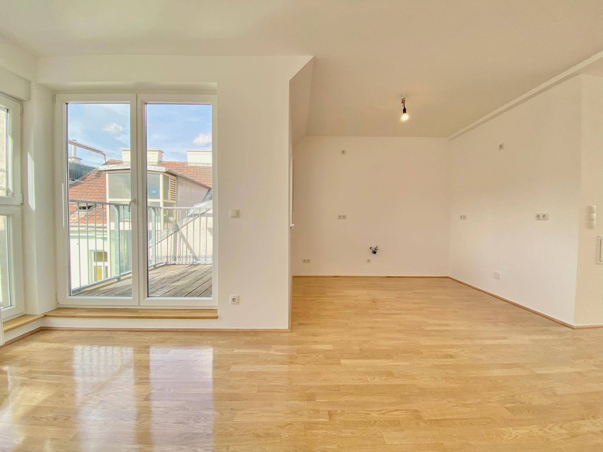 Offener Wohnbereich mit Parkettboden und großen Fenstern, die den Zugang zum Balkon ermöglichen.