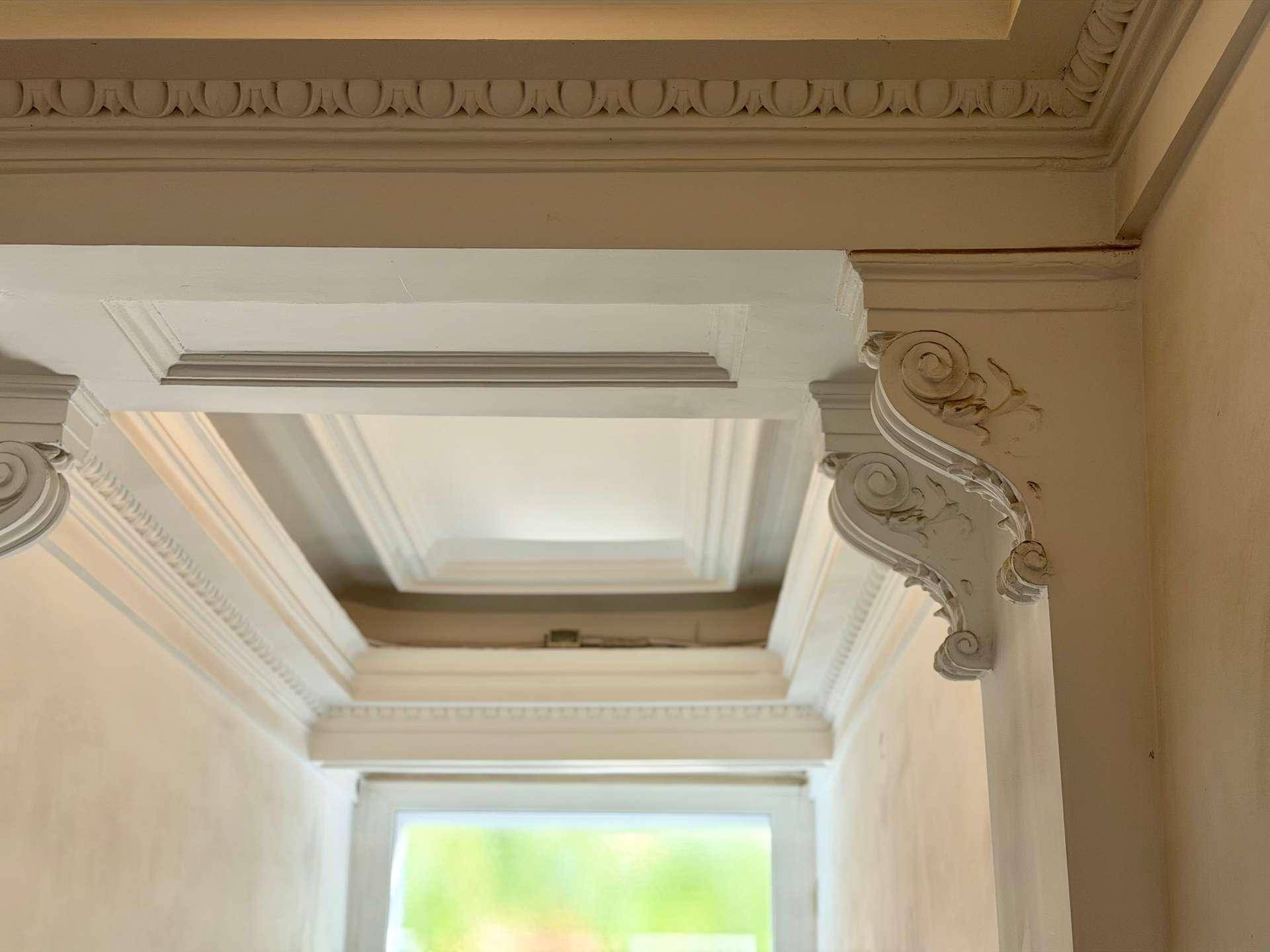 Detailaufnahme der kunstvollen Stuckverzierungen an der Decke und den Wänden des Flurs.