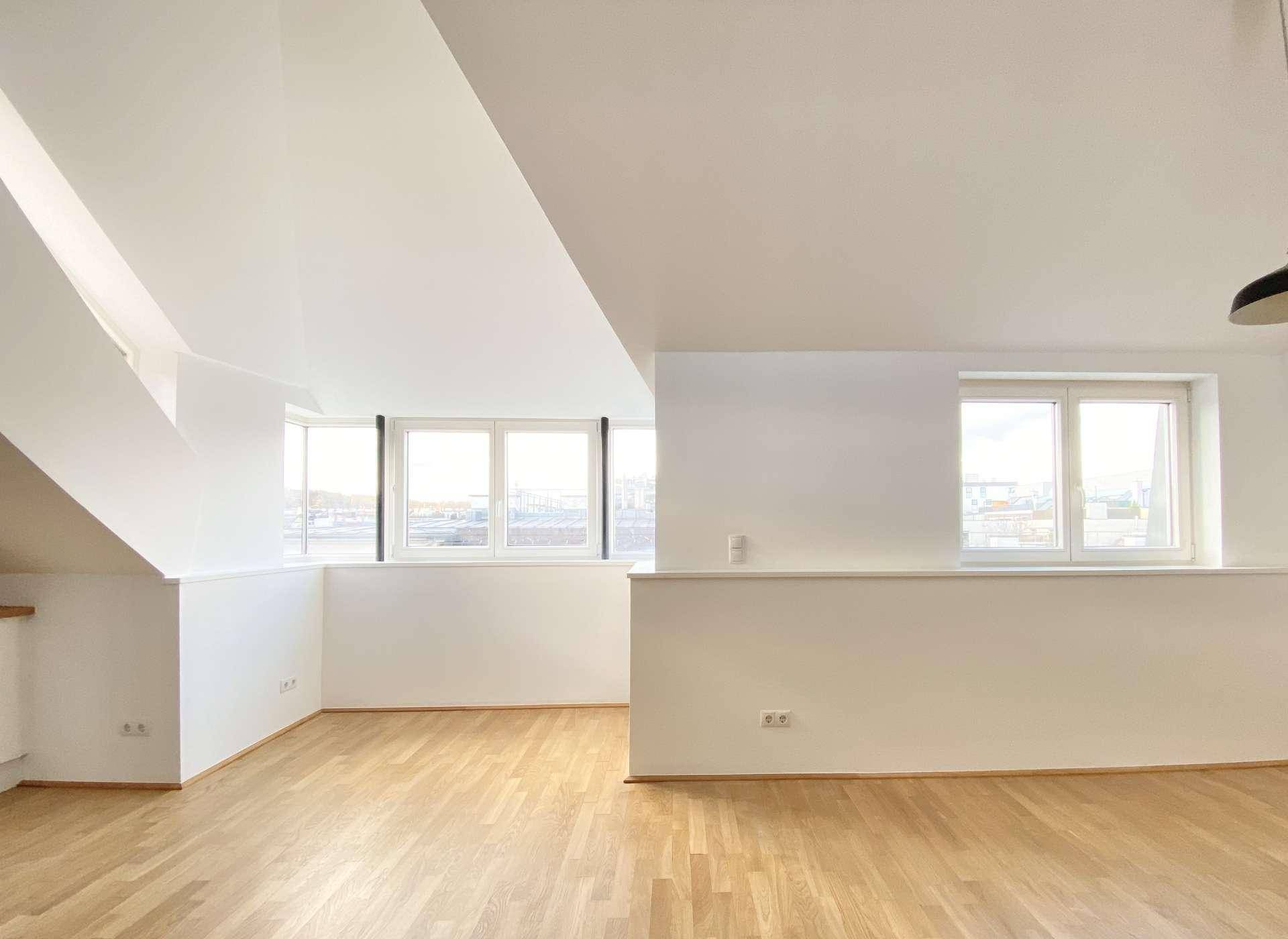 Heller Wohnbereich mit Holzboden, schrägen Decken und großen Fenstern mit Stadtblick.