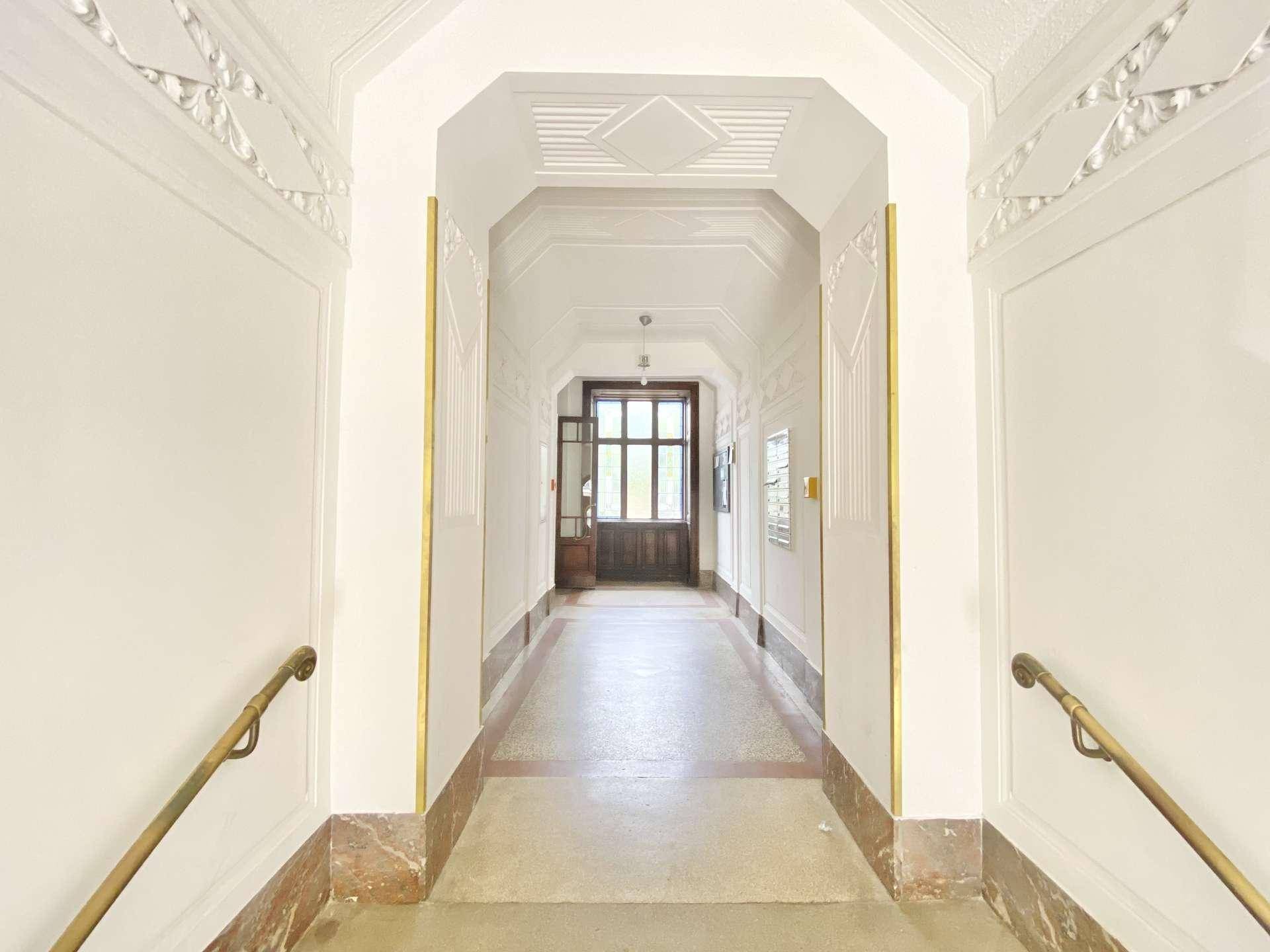 Eleganter Flur mit hohen Decken, Stuckverzierungen und Marmorboden in einem Altbau.