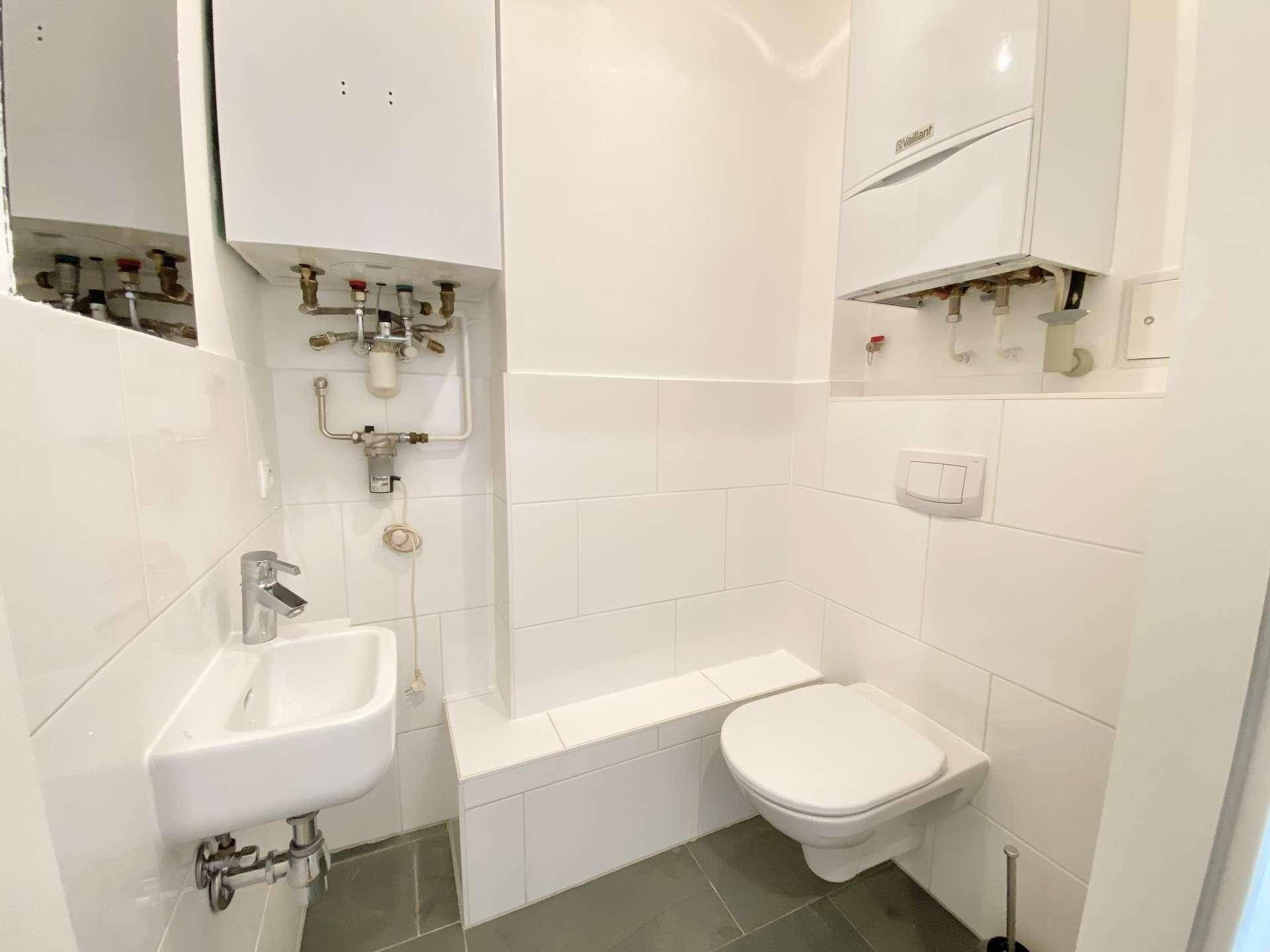 Kleines Gäste-WC mit wandhängendem WC, Waschbecken und sichtbarer Heizungsanlage.