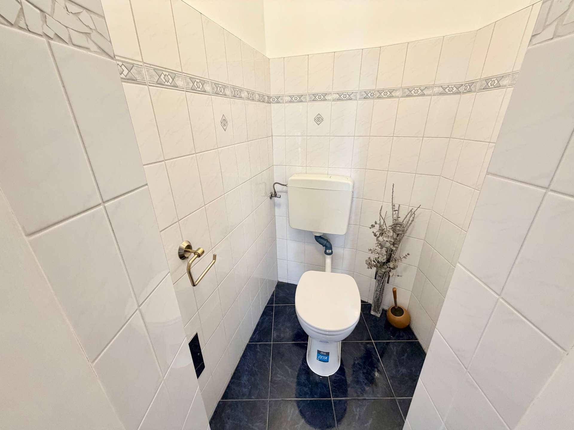 Separate Toilette mit weißen Wandfliesen und dunklem Boden, einfach und funktional.