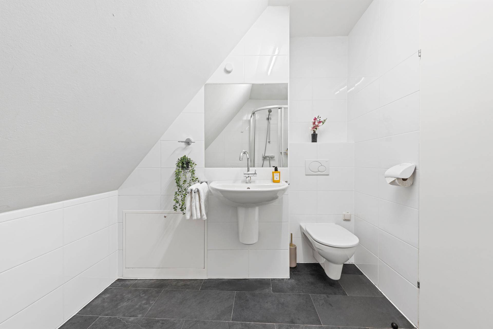 Modernes Badezimmer im Dachgeschoss mit Dusche, Waschbecken und dunklem Fliesenboden.