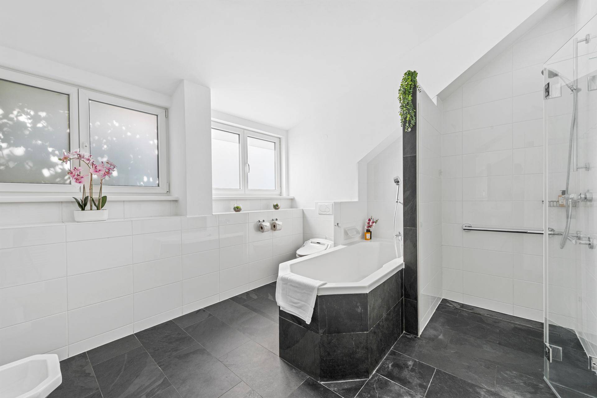 Geräumiges Badezimmer mit Badewanne, Dusche, Bidet und großen Fenstern.