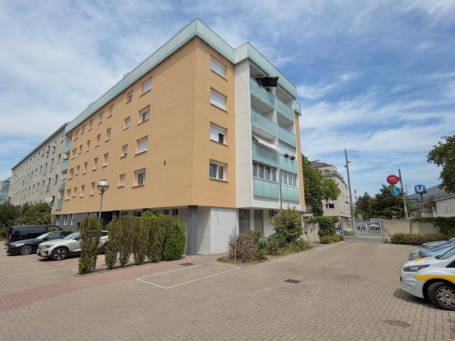 Mehrfamilienhaus mit moderner Fassade, Balkonen und Außenparkplätzen unter blauem Himmel.