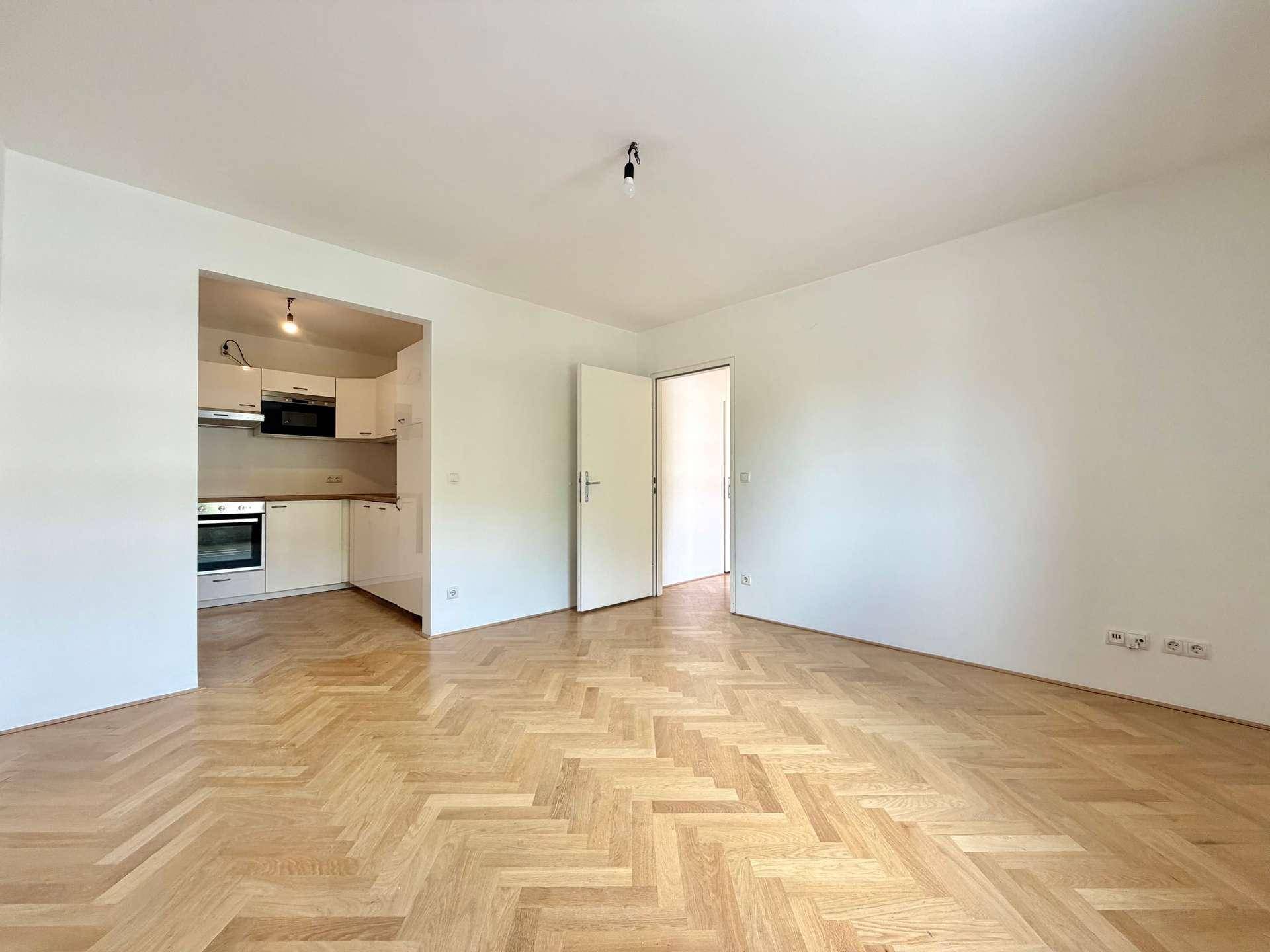 Offener Wohnbereich mit Fischgrätparkettboden und integrierter Küchenzeile, ideal für modernes Wohnen.