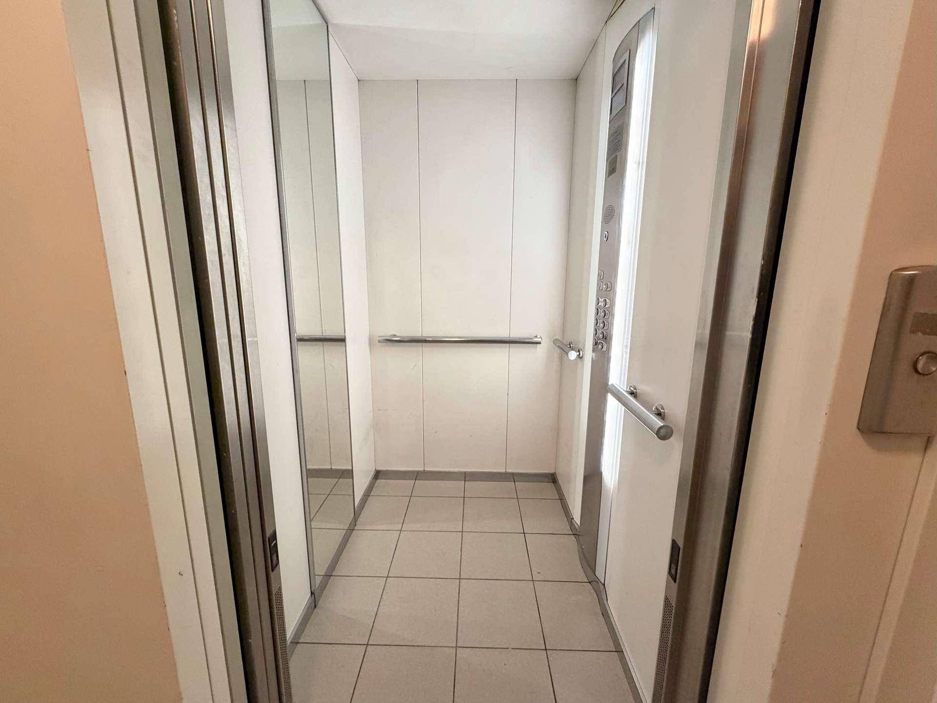 Moderner Aufzug mit Spiegelwand und Edelstahlhandlauf, der eine saubere Kabine zeigt.