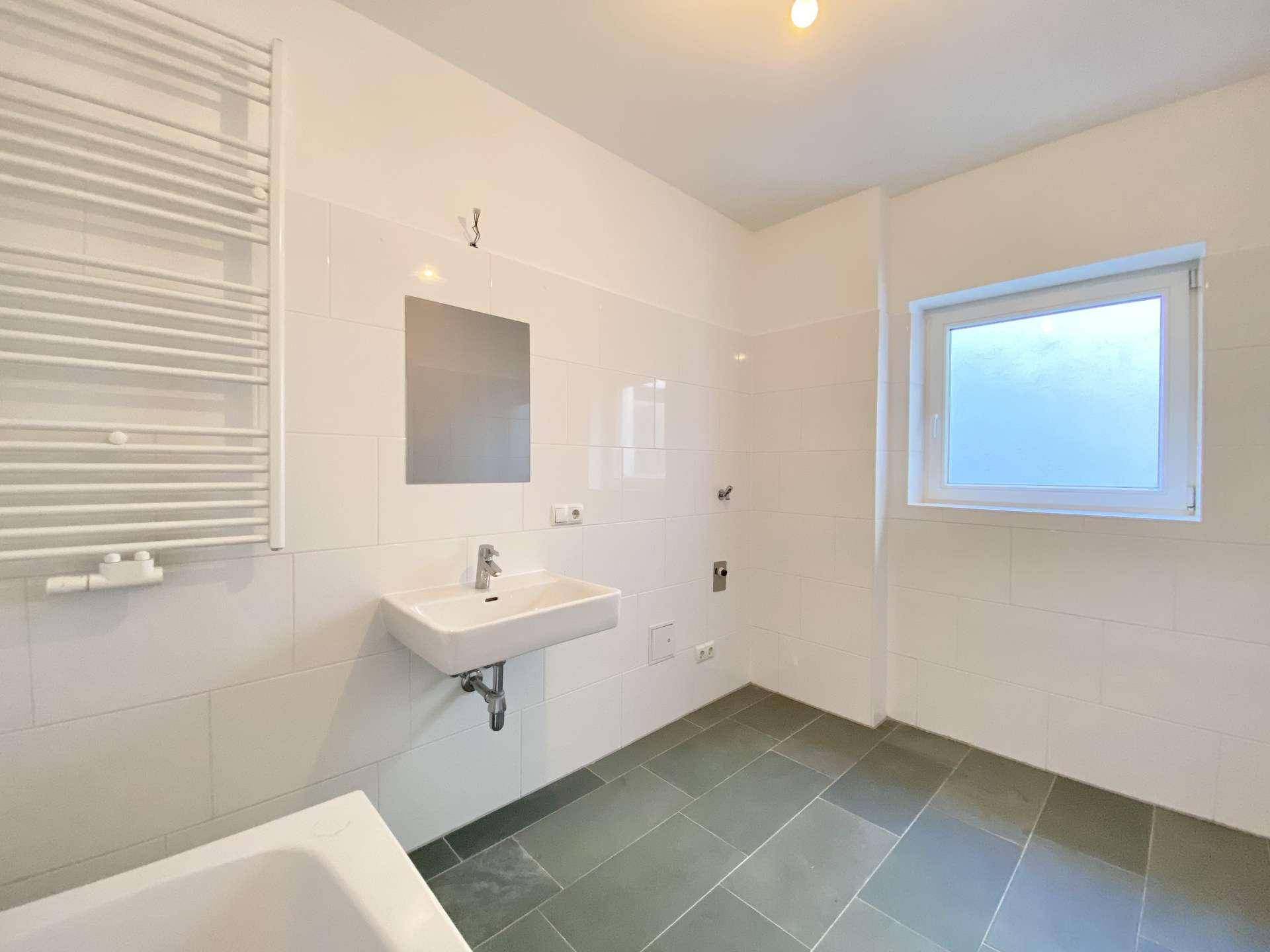 Modernes Badezimmer mit weißen Fliesen, Waschbecken, Handtuchheizkörper und Fenster.