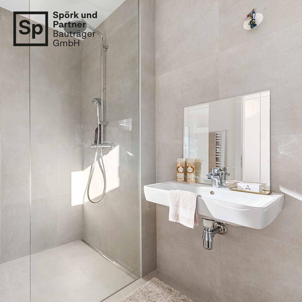 Modernes Badezimmer mit begehbarer Dusche, hellem Waschbecken und grauen Fliesen.