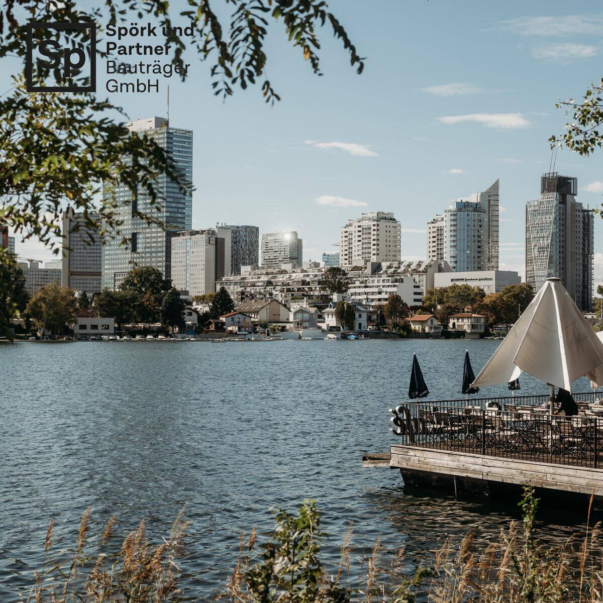 Blick über einen See auf die Wiener Skyline mit einem schwimmenden Restaurant im Vordergrund.