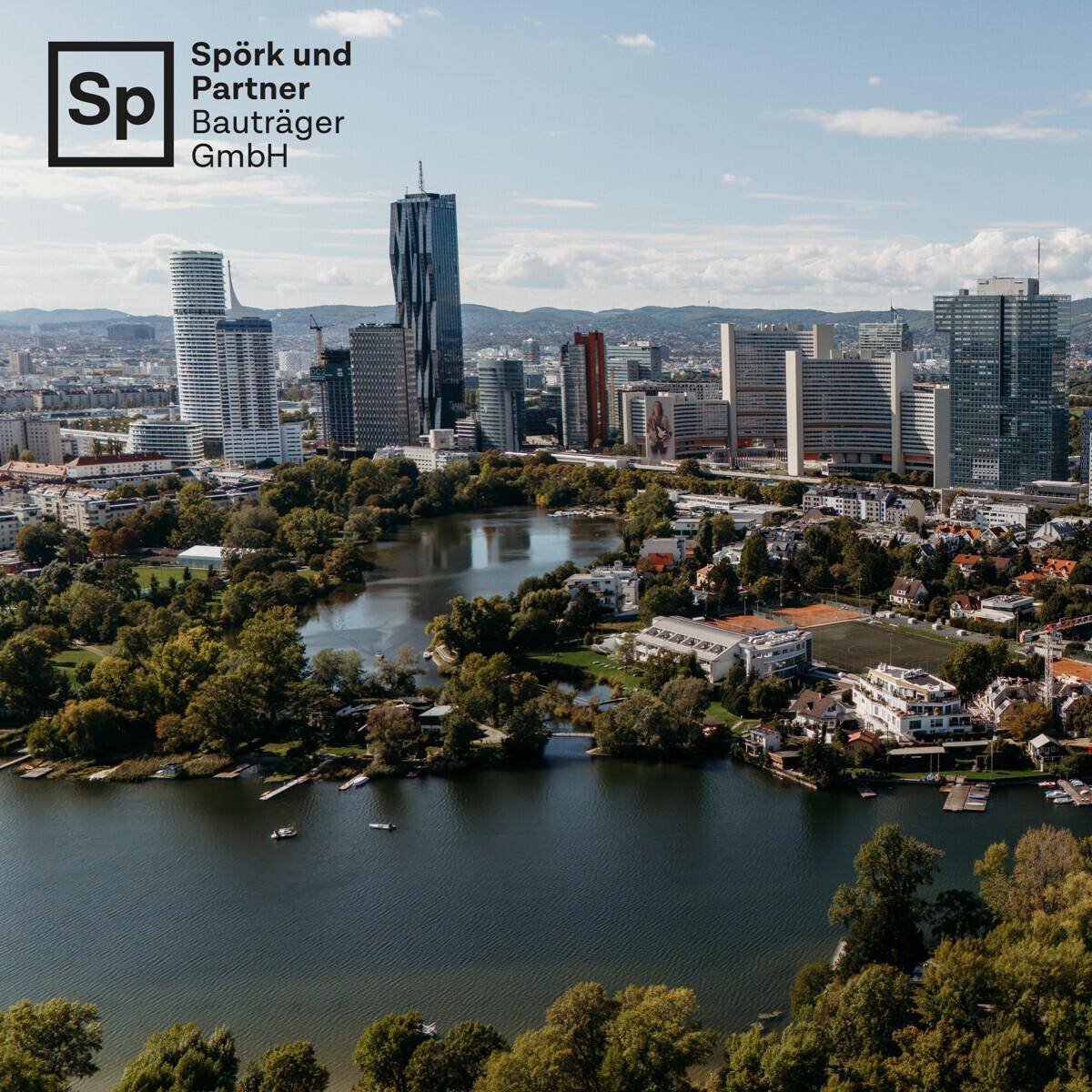 Panoramablick auf eine Stadtlandschaft mit Hochhäusern, einem See und grünen Ufern.
