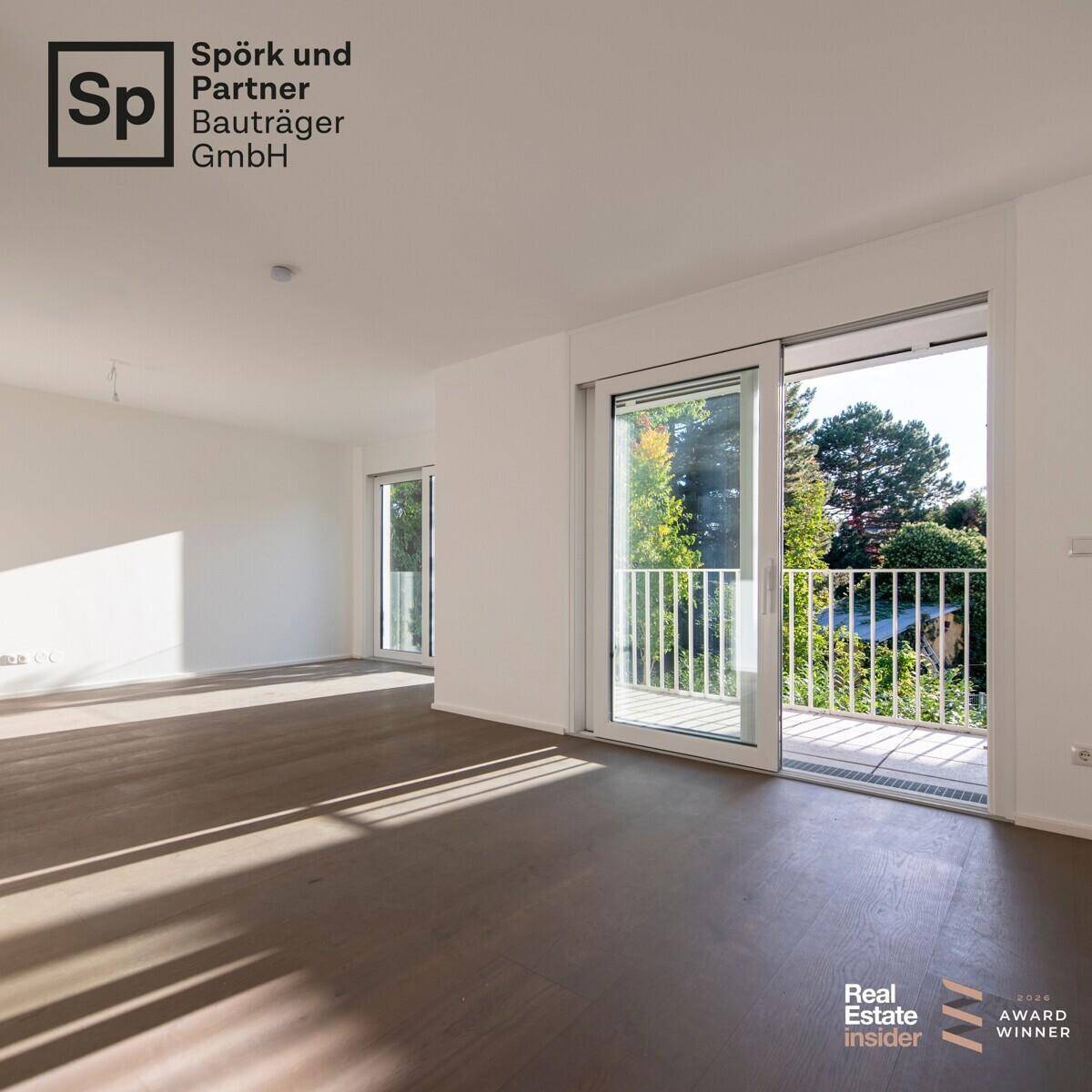 Geräumiger, heller Raum mit dunklem Holzboden und Zugang zum Balkon.
