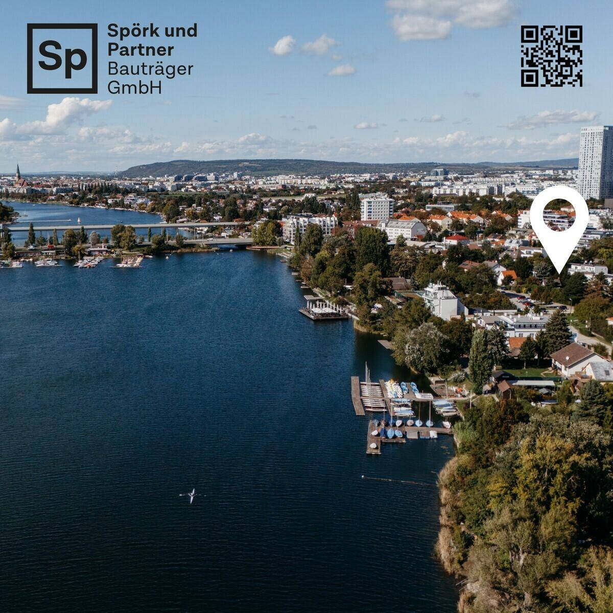 Luftaufnahme einer Stadtlandschaft mit See, Gebäuden und einem markierten Standort.