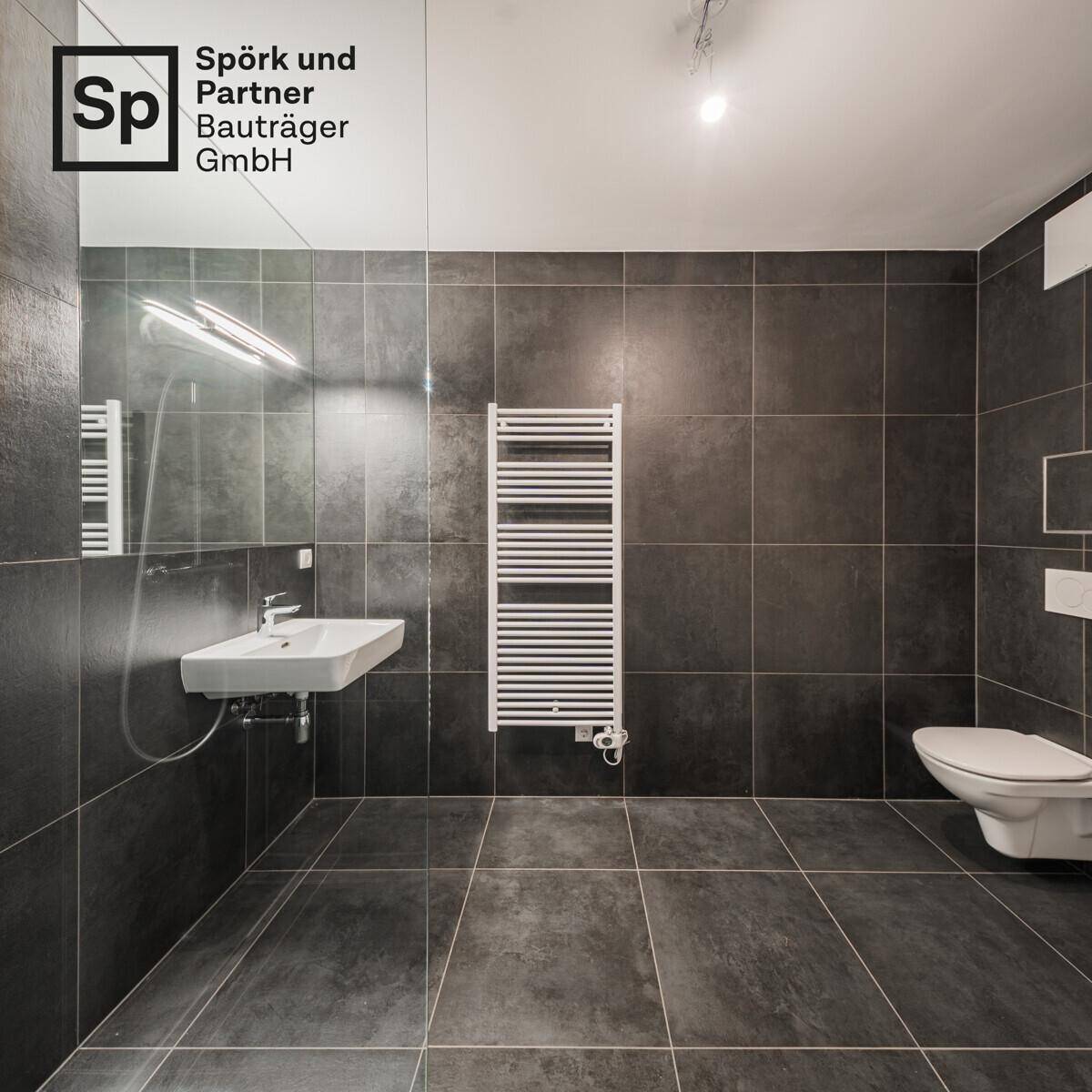 Modernes Badezimmer mit dunklen Fliesen, Waschbecken und wandhängendem WC.