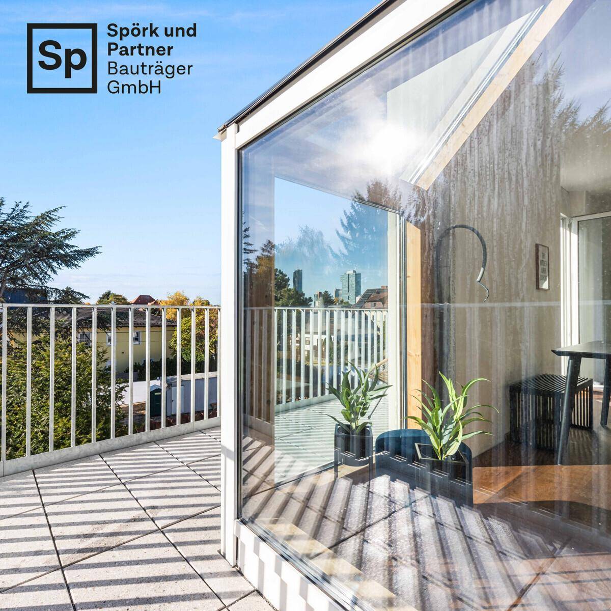 Sonniger Balkon mit Fliesenboden und großen Glasflächen, die die Umgebung widerspiegeln.