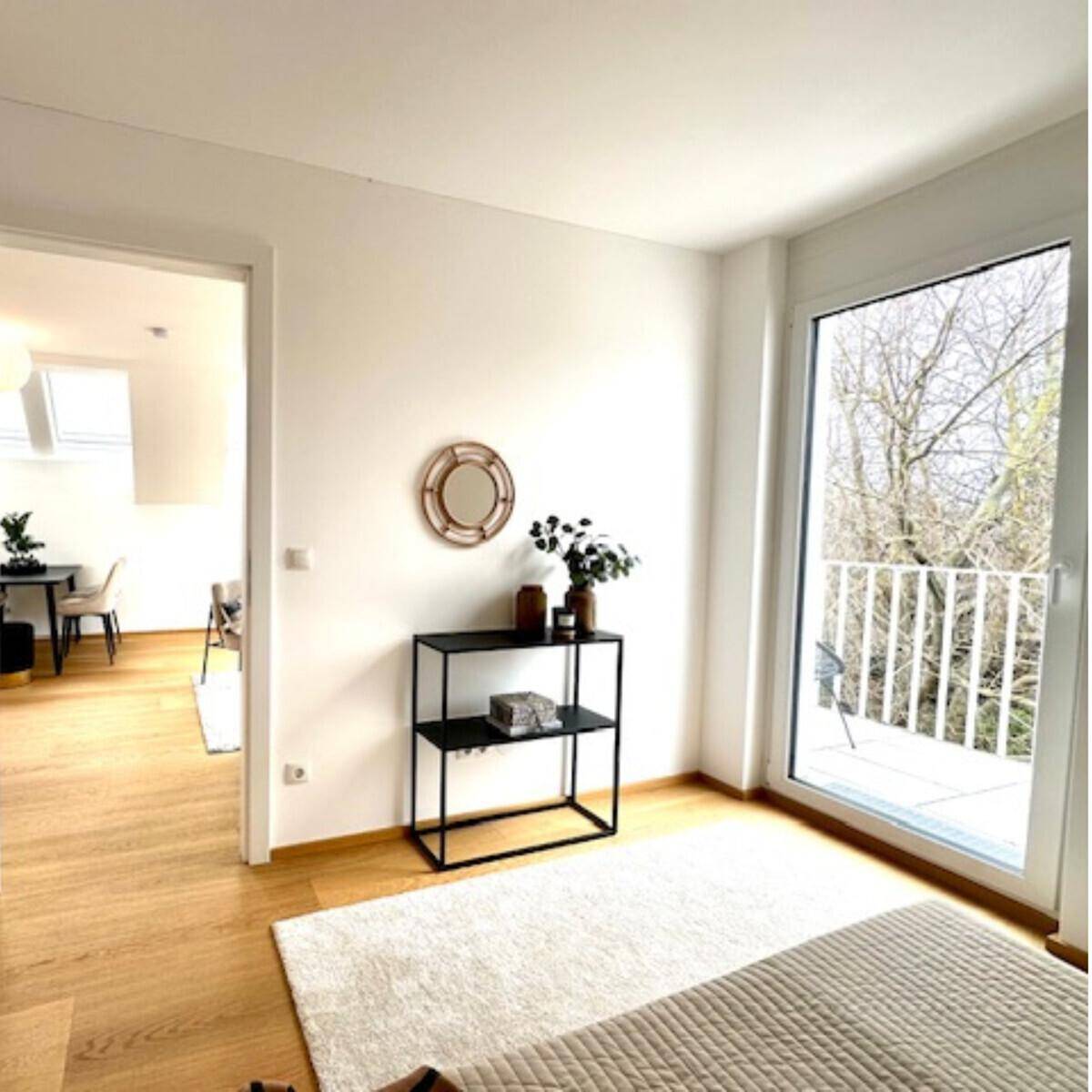 Helles Schlafzimmer mit Holzboden, großem Fenster und Zugang zu einem französischen Balkon.