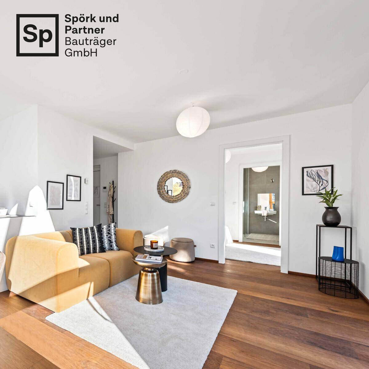 Helles Wohnzimmer mit Holzboden und Blick in ein angrenzendes modernes Badezimmer.