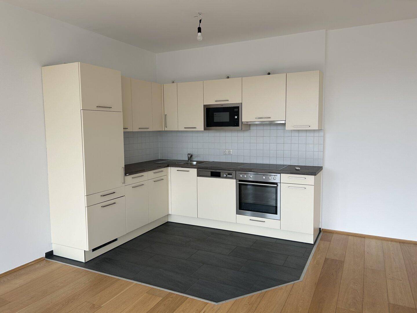 Funktionale L-förmige Einbauküche in hellem Beige mit modernen Geräten und Fliesenrückwand.
