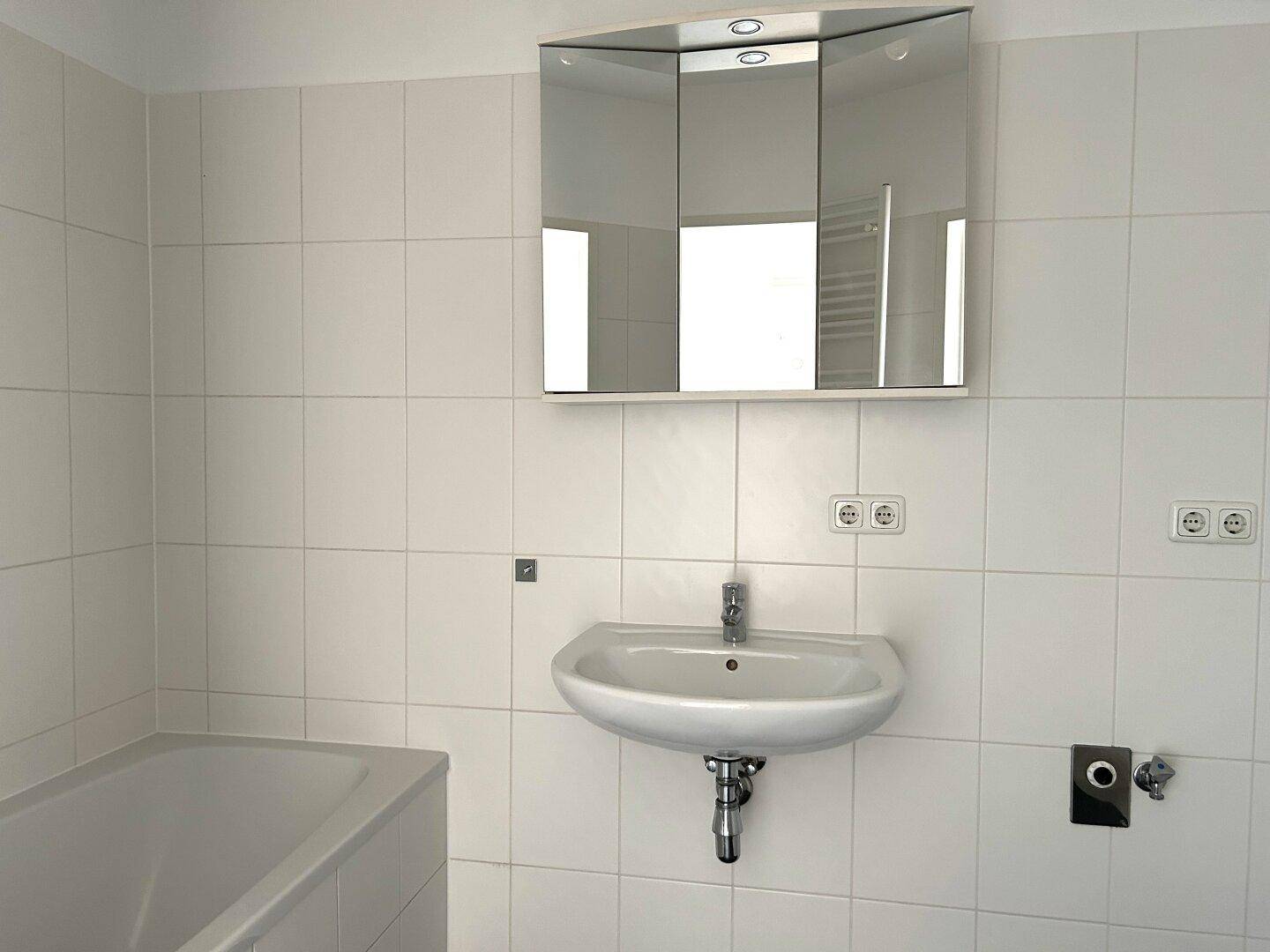 Helles Badezimmer mit Badewanne, Waschbecken und Spiegelschrank, komplett gefliest.
