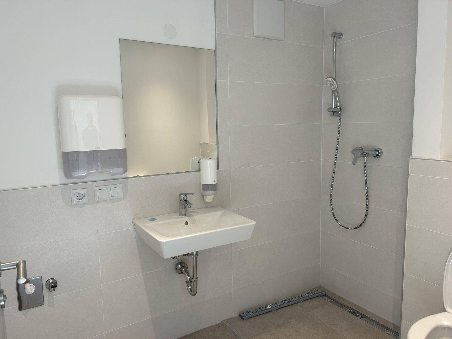 Modernes Badezimmer mit Duschbereich, Waschbecken und großem Spiegel in hellen Fliesen.