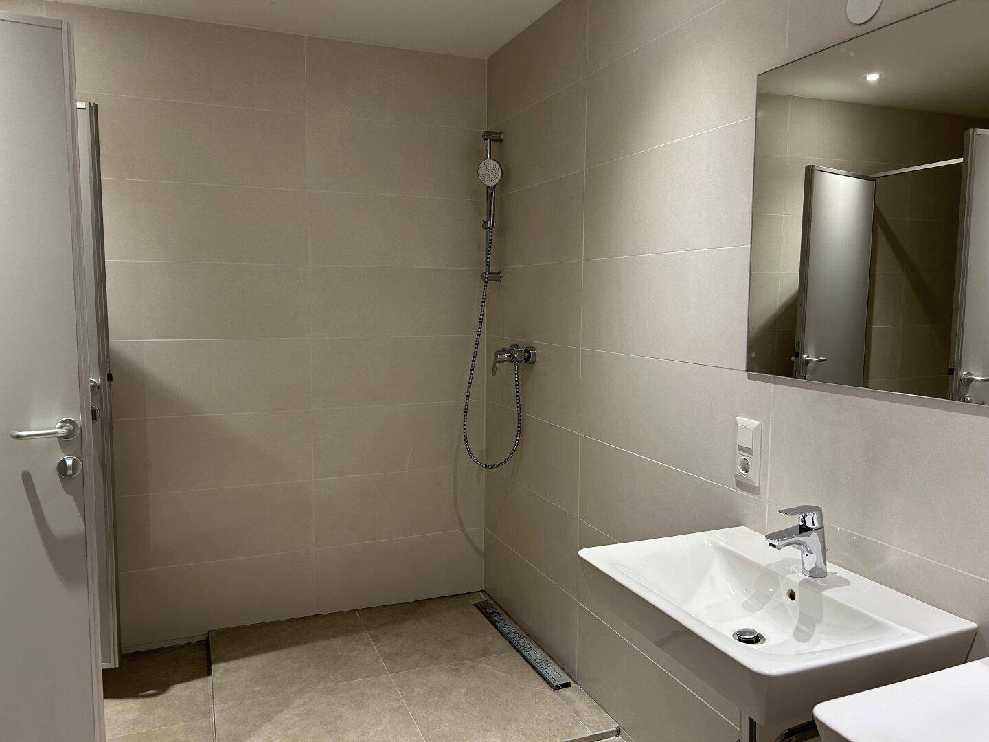 Modernes Badezimmer mit beigefarbenen Großformatfliesen, Duschbereich und elegantem Waschbecken.