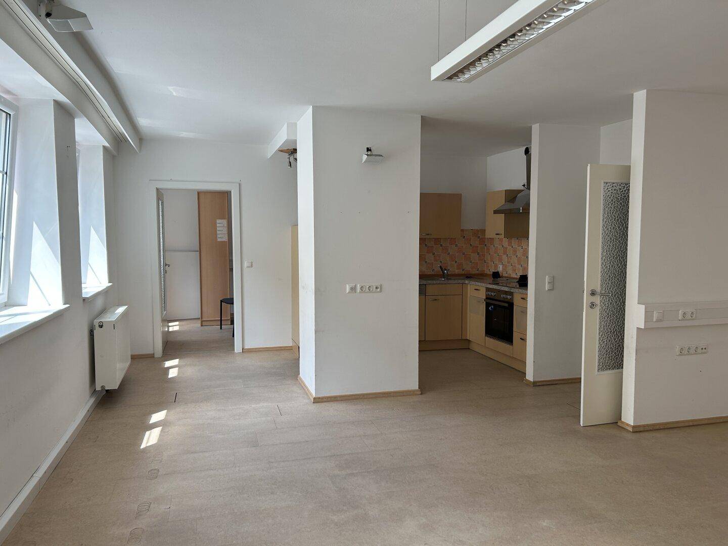 Helles, offenes Zimmer mit Blick auf eine integrierte Küchenzeile und großen Fenstern.