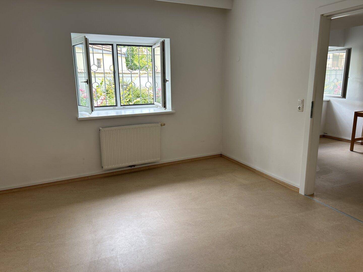 Helles Zimmer mit einem Fenster, das einen Blick ins Grüne bietet, und Heizkörper.