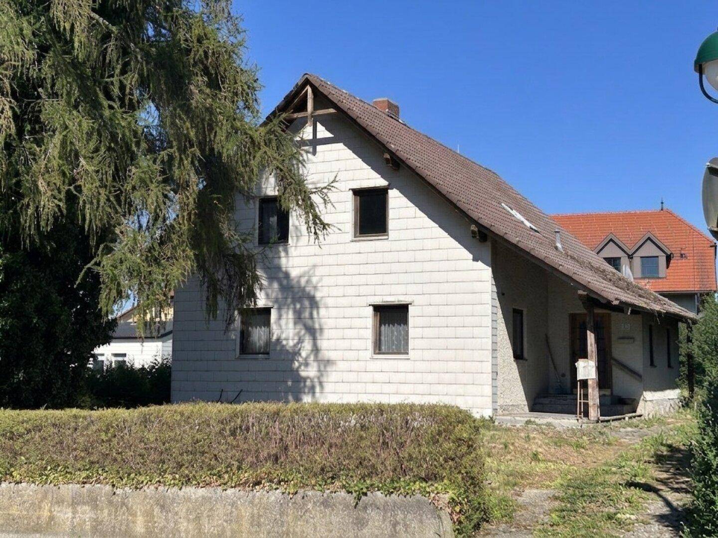 Freistehendes Einfamilienhaus mit heller Fassade und braunem Ziegeldach in ländlicher Umgebung.