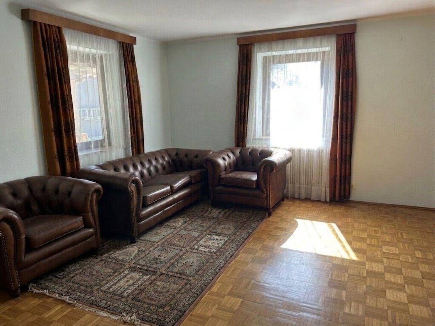 Helles Wohnzimmer mit klassischem Ledersofa, gemustertem Teppich und Fischgrätparkettboden.