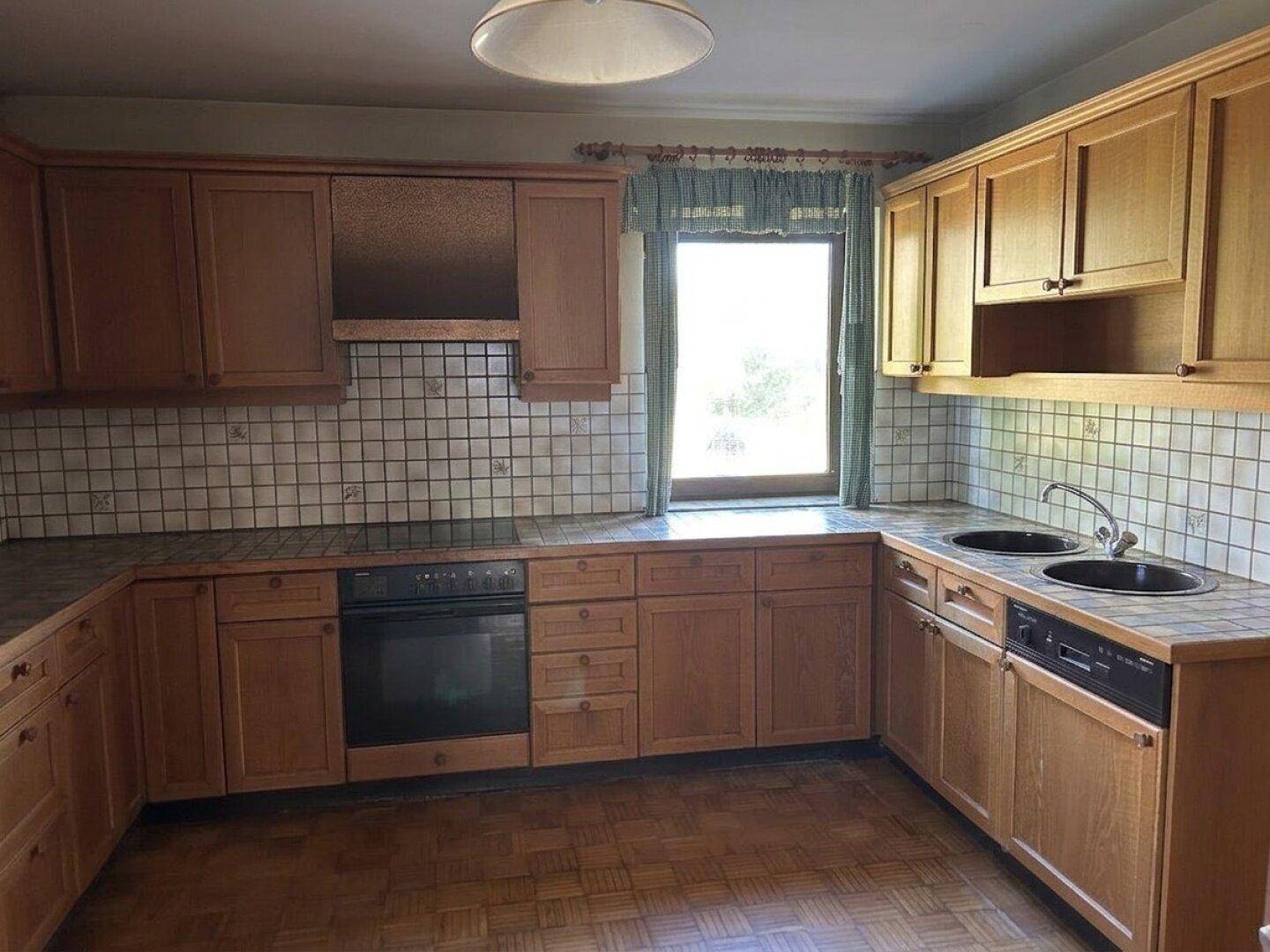 Funktionale Küche mit Holzschränken, gefliestem Spritzschutz und integrierten Elektrogeräten.