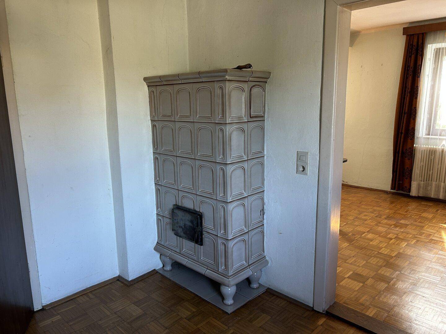 Detailansicht eines traditionellen, verzierten Kachelofens in einem Wohnbereich mit Parkettboden.