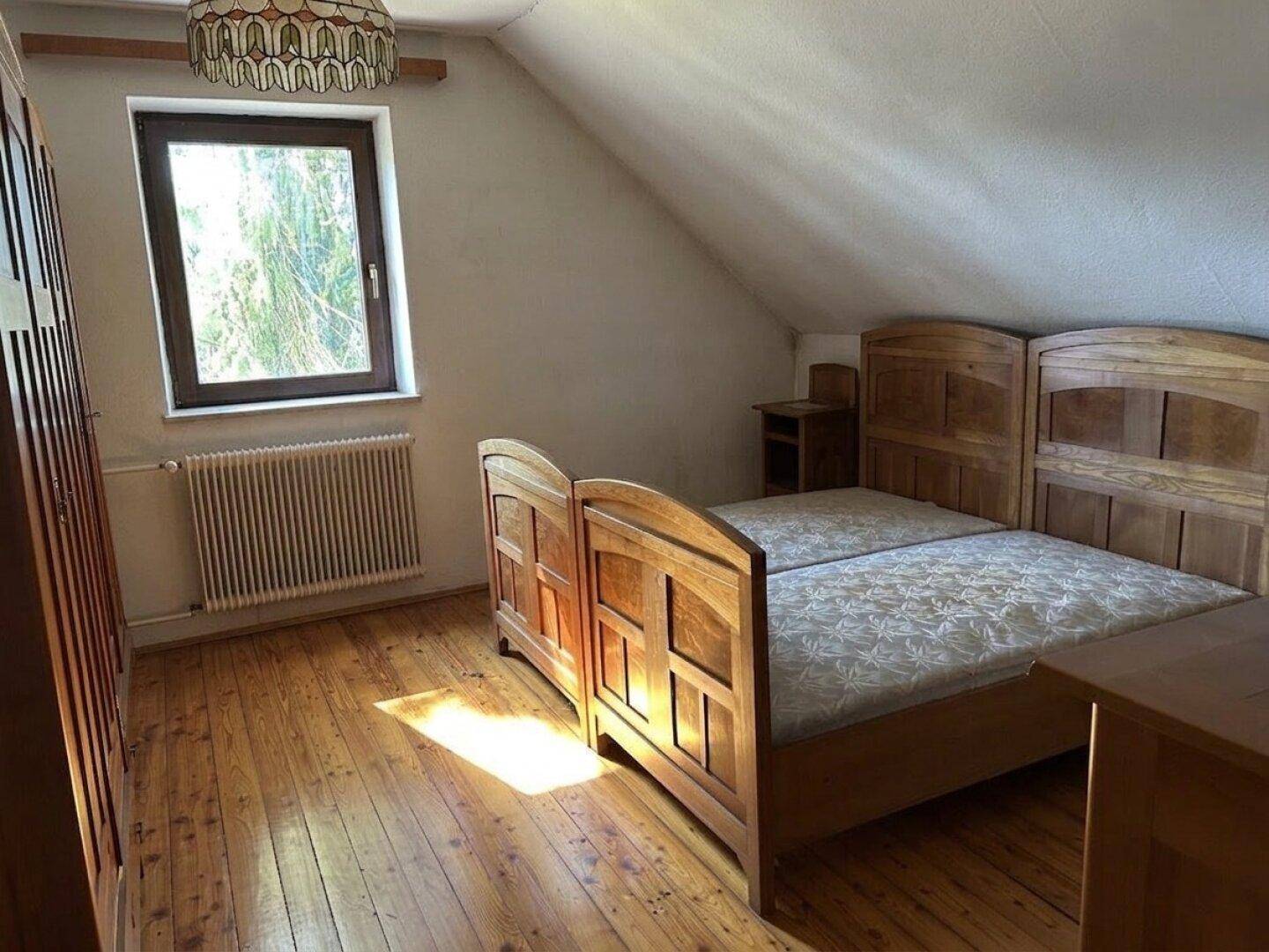 Schlafzimmer im Dachgeschoss mit Holzboden, schrägen Wänden und einem Doppelbett aus Holz.