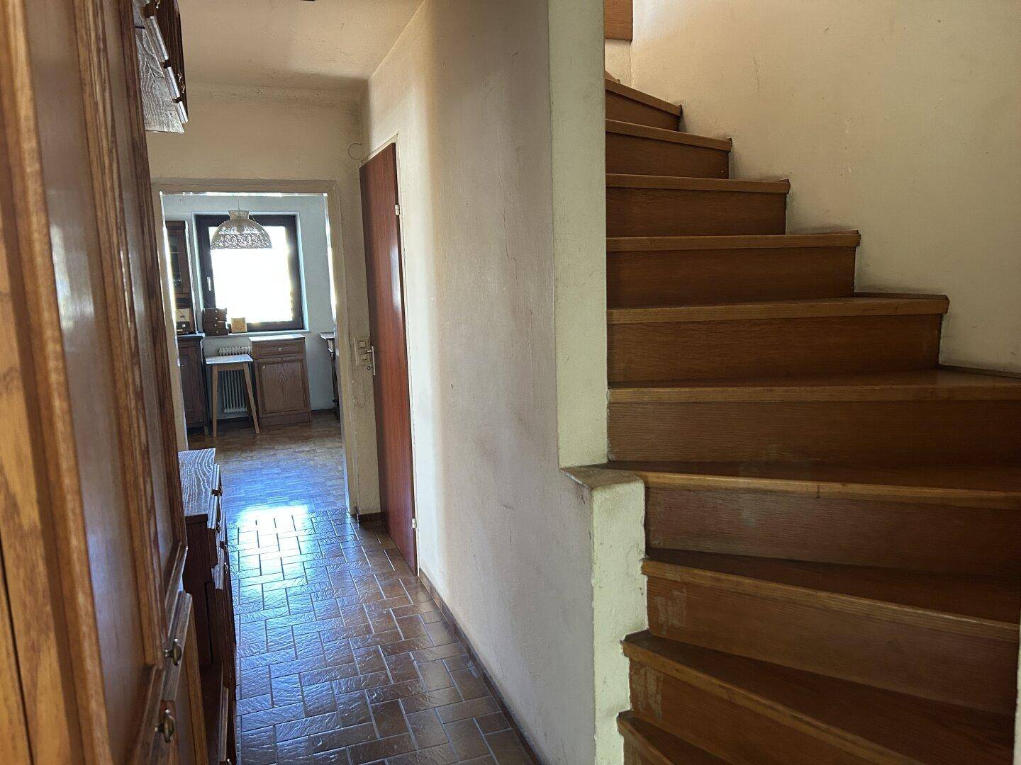 Heller Flur mit Holztreppe, Terrakotta-Fliesenboden und Zugang zu weiteren Räumen.