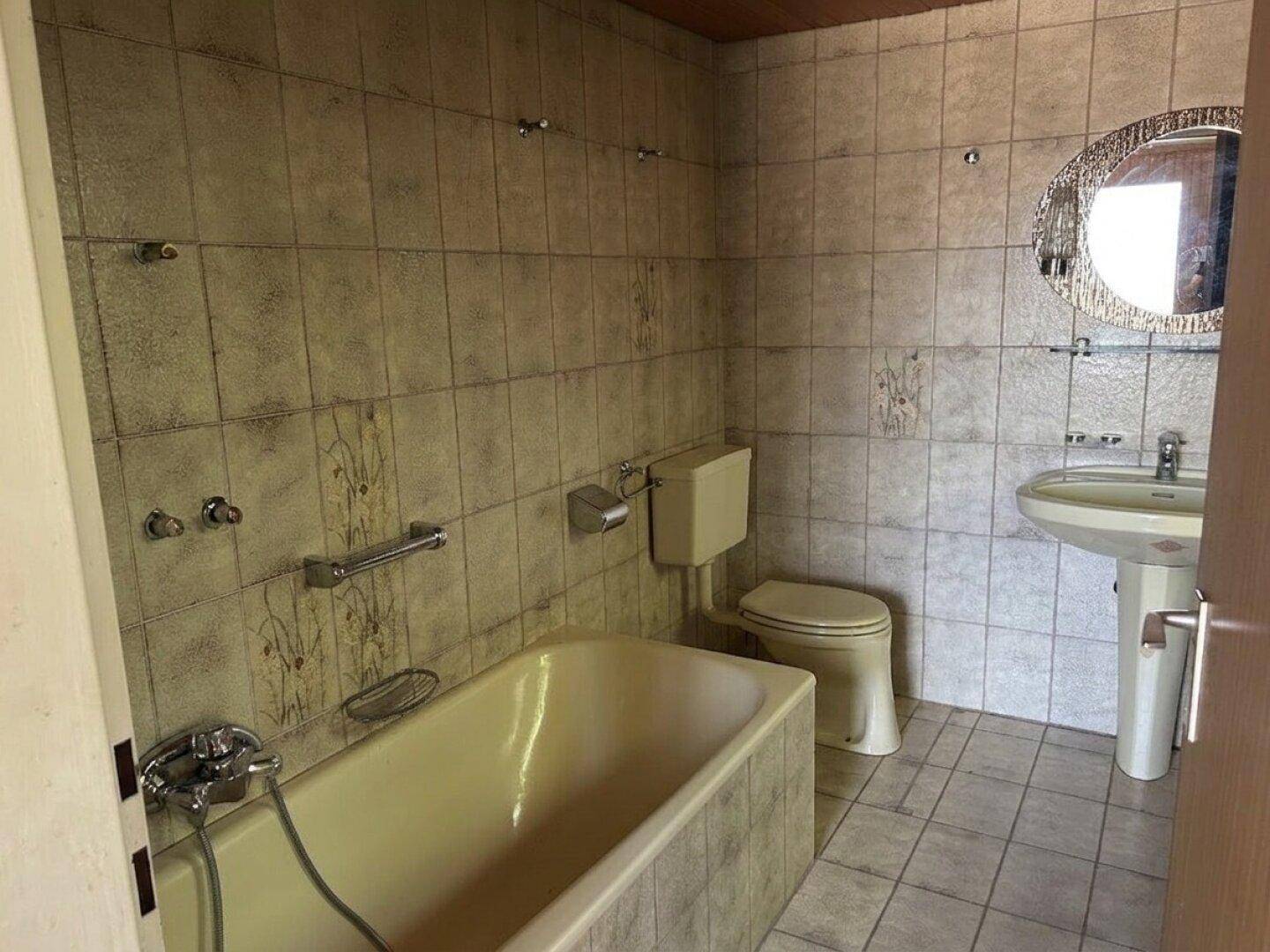 Badezimmer im Stil der 80er Jahre mit beigefarbenen Fliesen, Badewanne und Waschtisch.