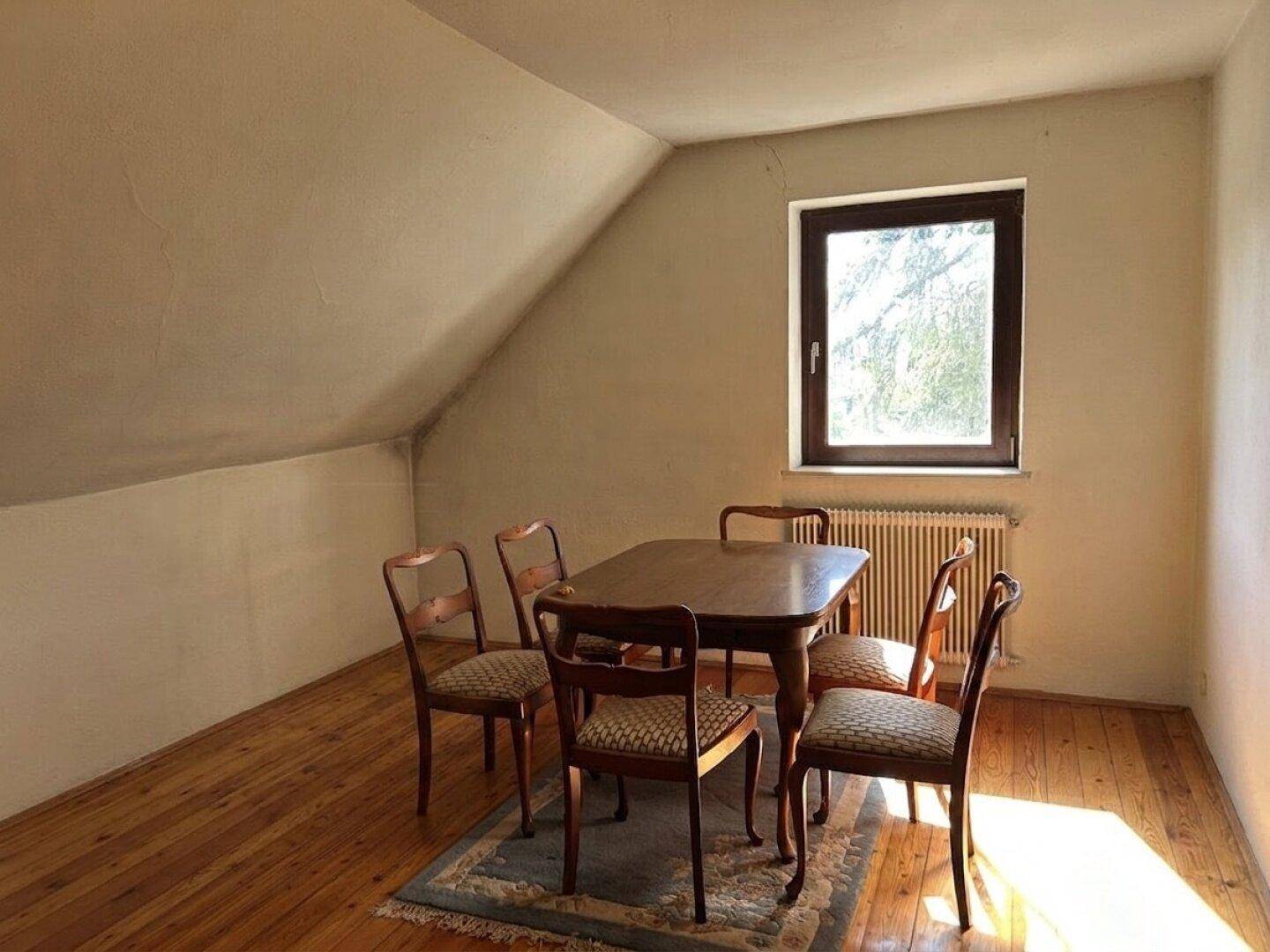 Gemütlicher Essbereich im Dachgeschoss mit Holzboden, schrägen Wänden und einem Fenster.