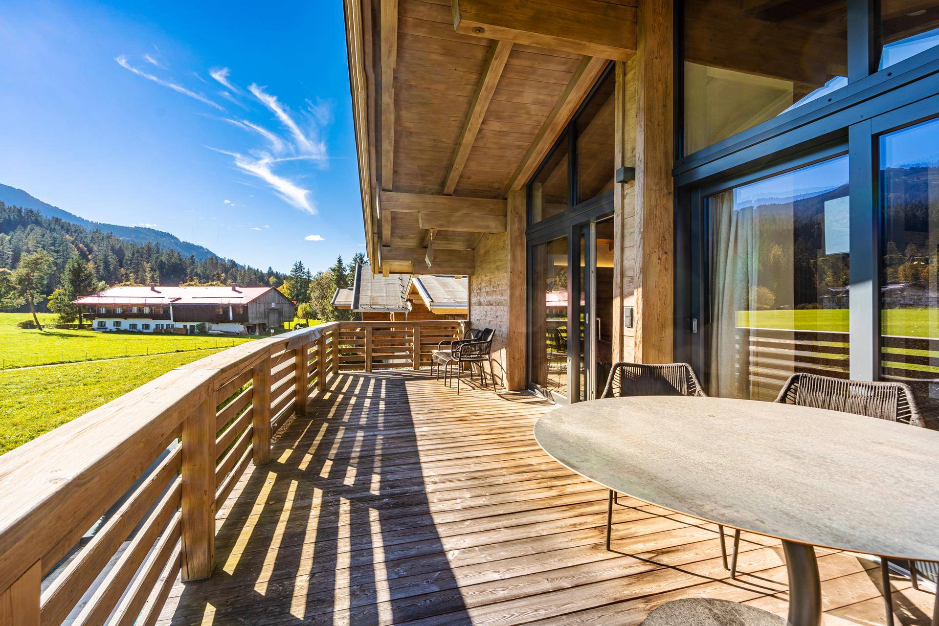 Geräumiger Holzbalkon mit Sitzgelegenheiten und weitem Blick über grüne Wiesen und Berge.