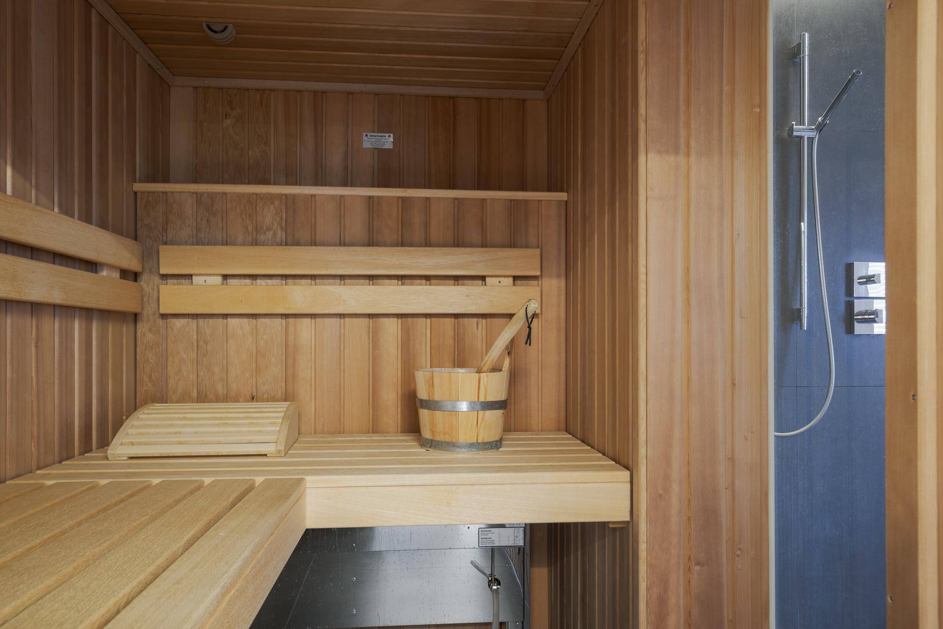 Detailansicht einer holzvertäfelten Sauna mit traditionellem Eimer und Schöpfkelle, direkt neben der Dusche.