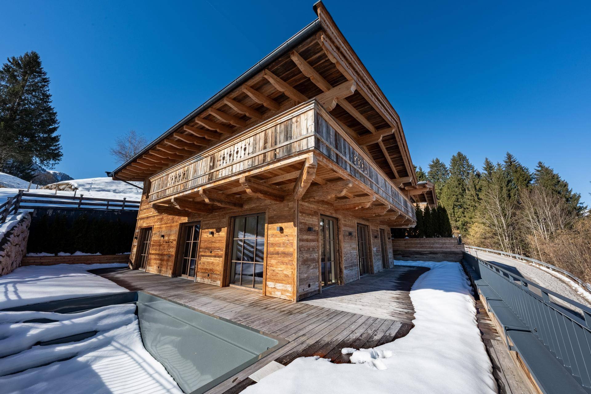 Holzfassade des Chalets mit großer Terrasse und integriertem Poolbereich im Winter.