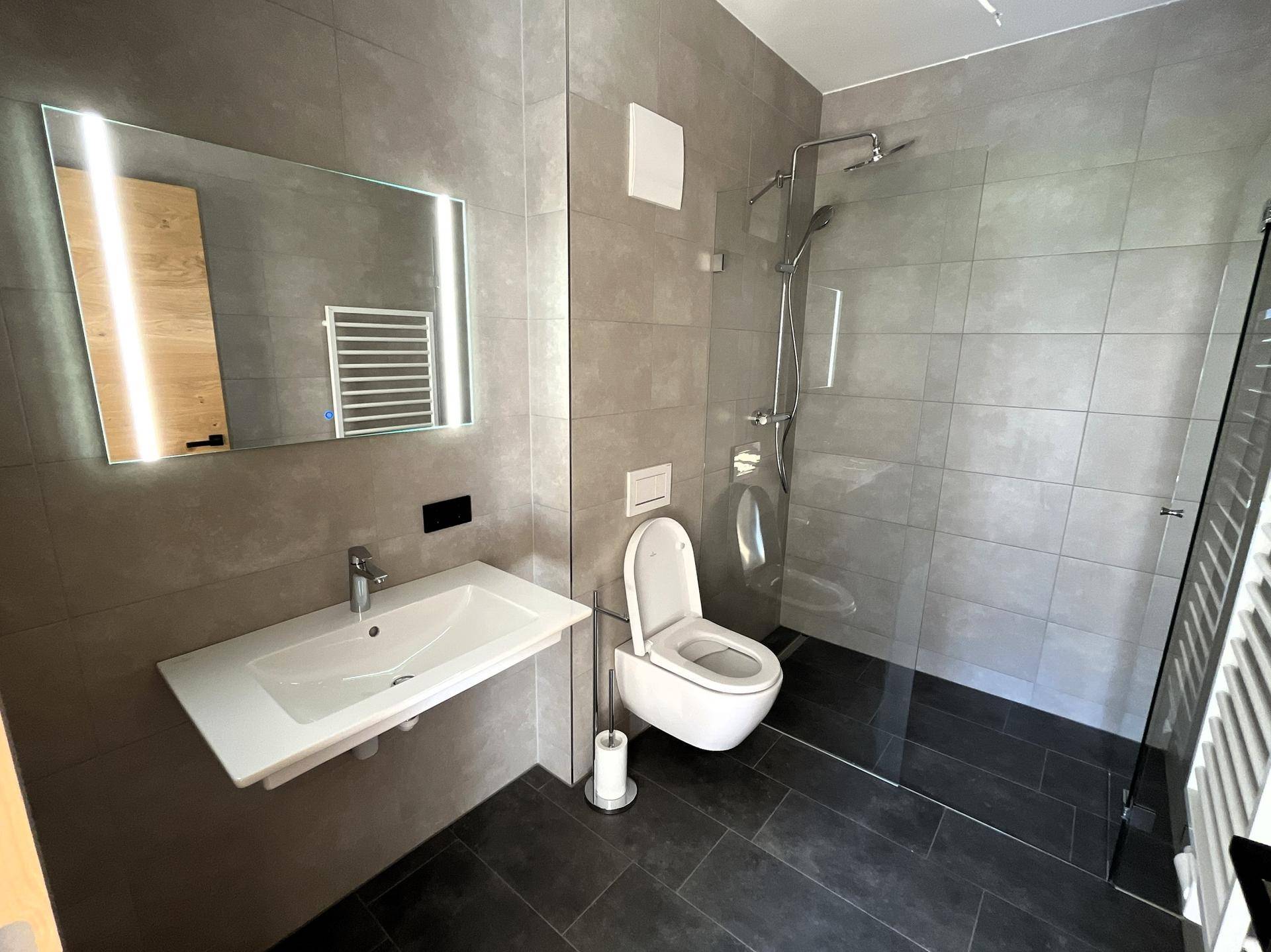 Modernes Badezimmer mit grauen Fliesen, ebenerdiger Dusche, Wand-WC und beheiztem Handtuchhalter.