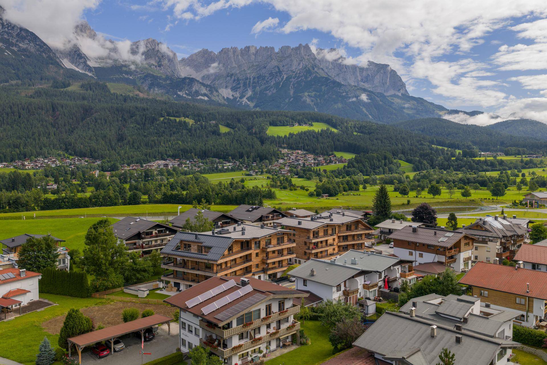 Weitläufige Luftaufnahme einer Wohnsiedlung mit modernen Gebäuden und Bergblick, umgeben von Natur.