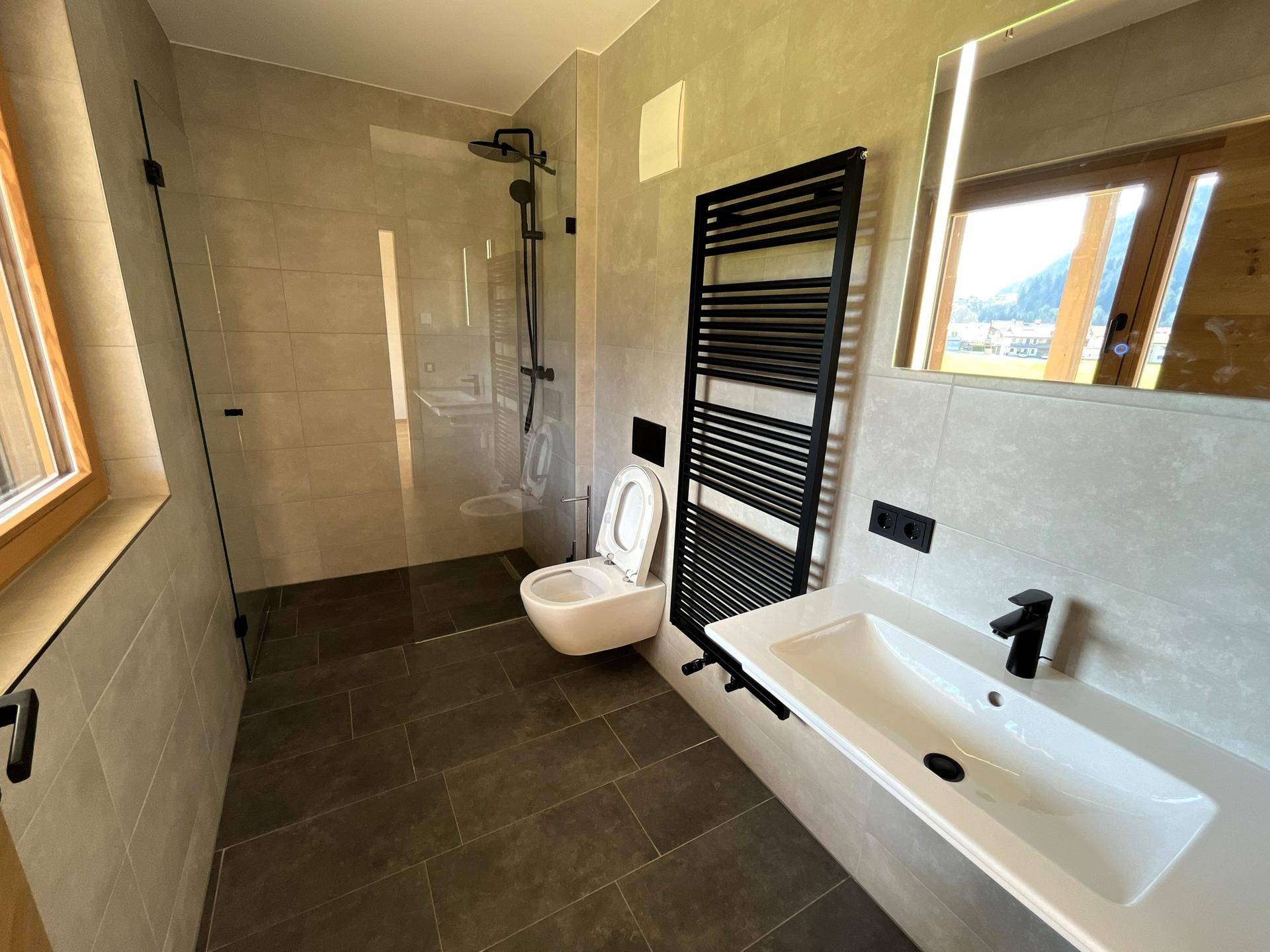 Modernes Badezimmer mit begehbarer Dusche, Wand-WC und beheiztem Handtuchhalter.