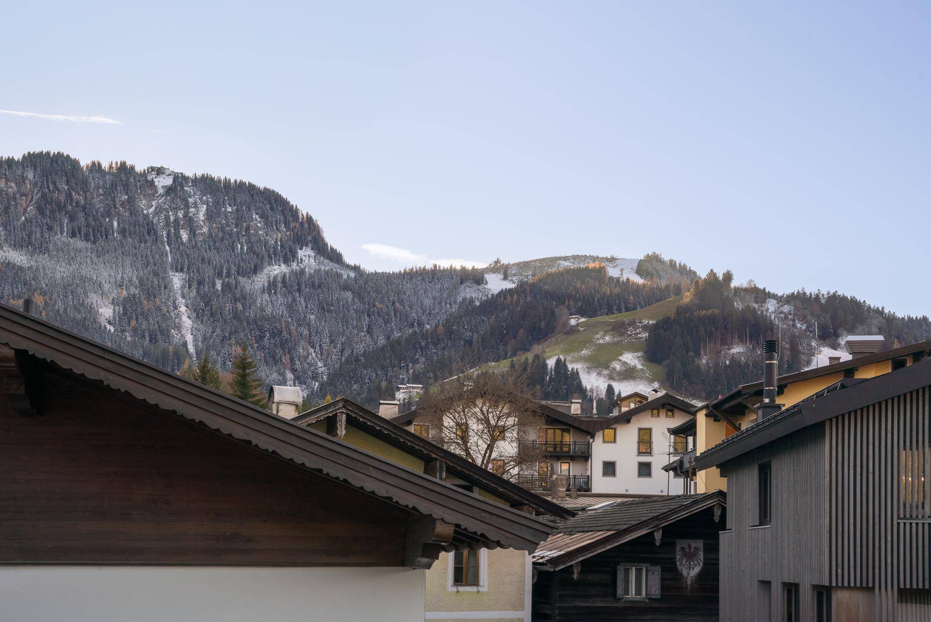 Malerische Berglandschaft mit schneebedeckten Gipfeln und bewaldeten Hängen, umgeben von traditionellen Häusern.