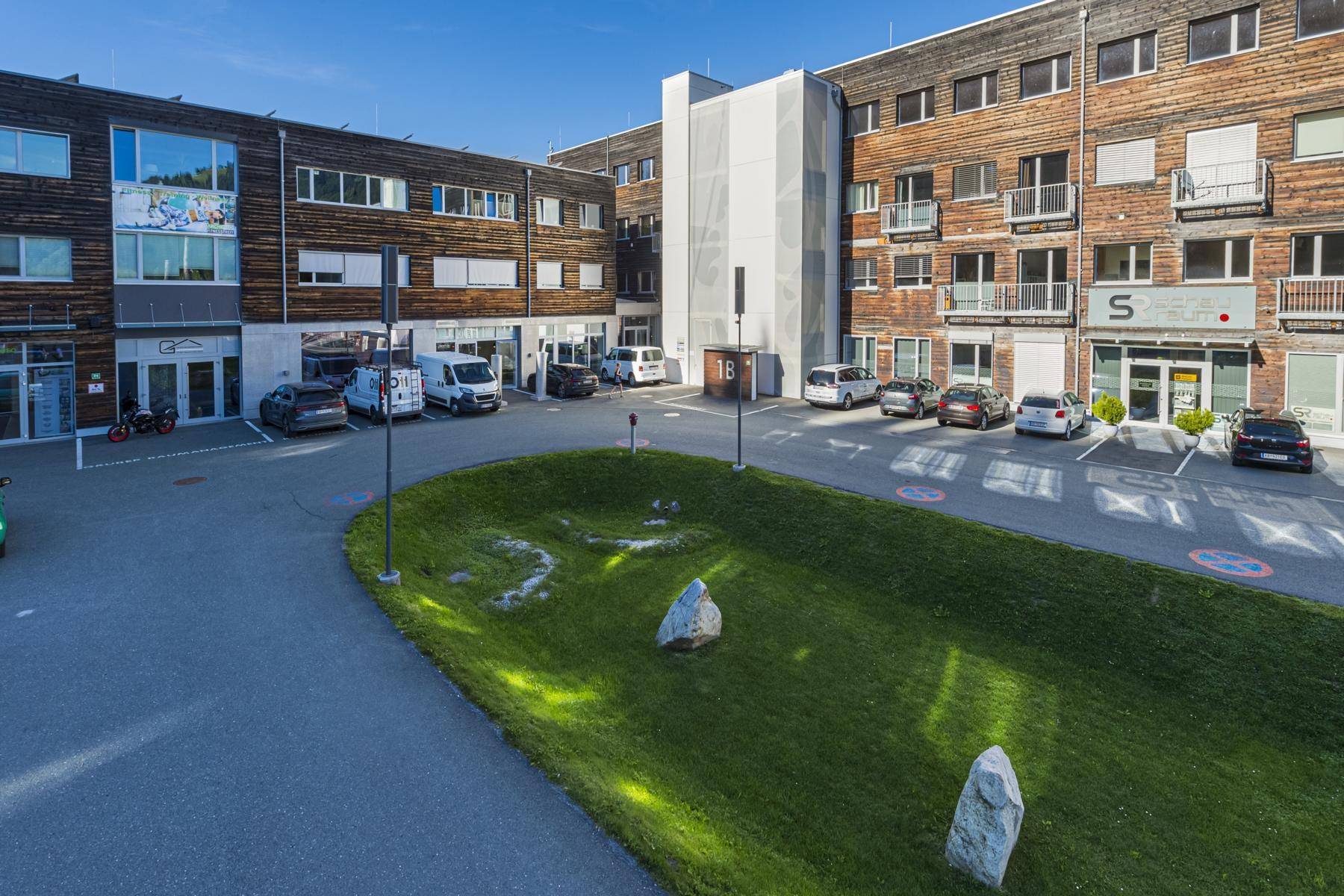 Ansicht eines modernen Gebäudes mit Holzfassade, Parkplätzen und gepflegten Grünflächen.