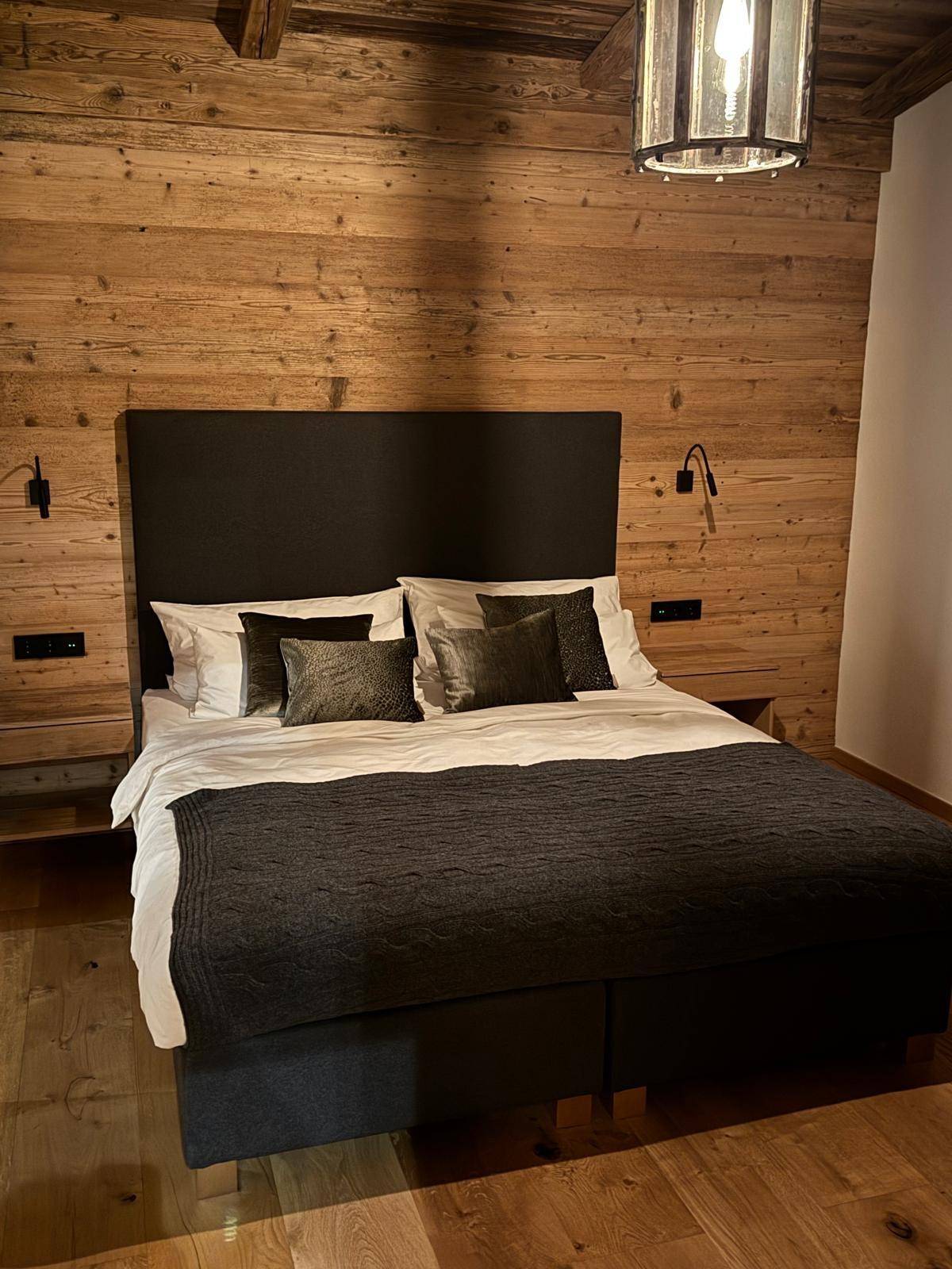 Komfortables Schlafzimmer mit Holzwänden, dunklem Bett und stilvoller Deckenbeleuchtung.