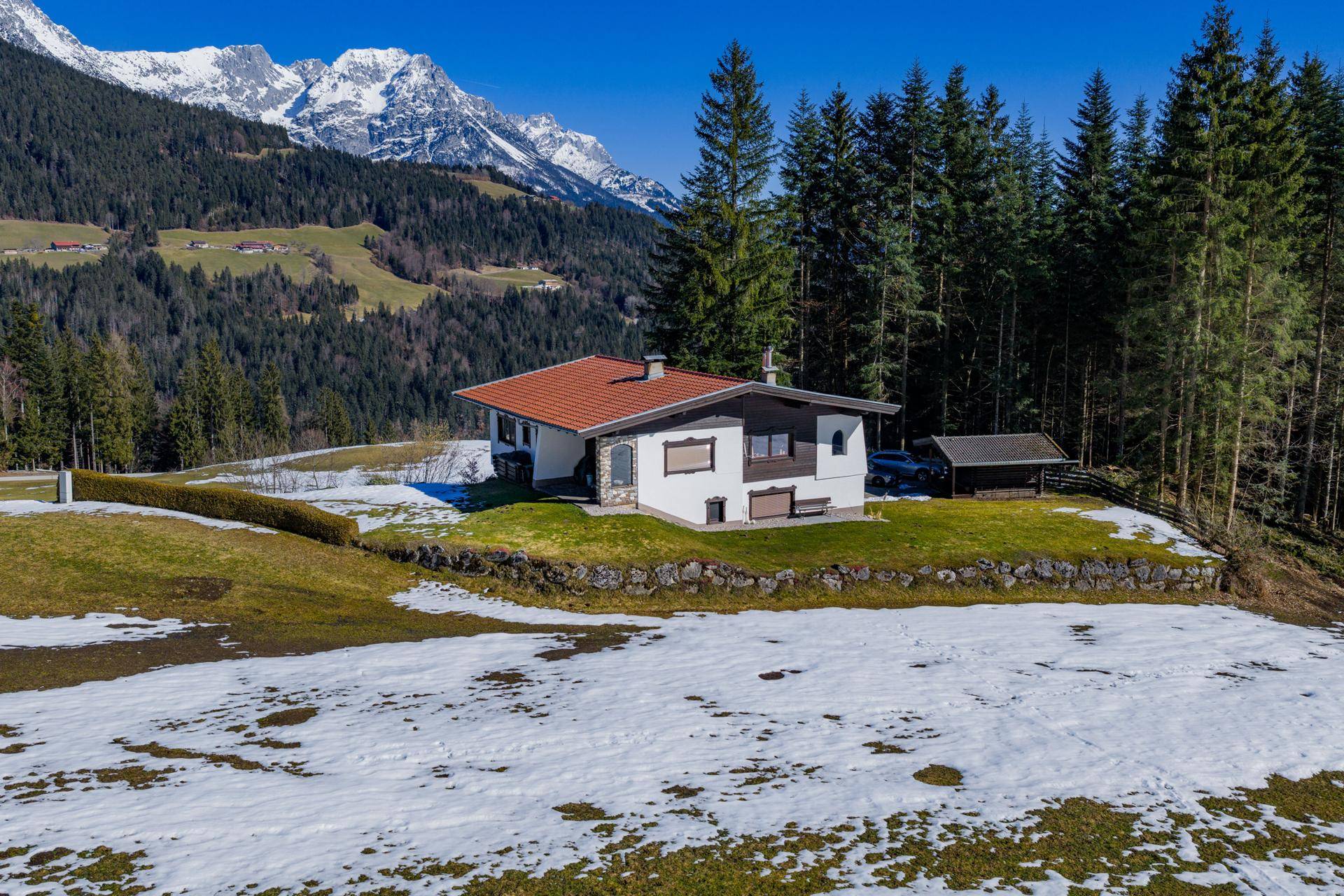 Das Haus von der Seite mit einem kleinen Schuppen und majestätischen Bergen im Hintergrund.